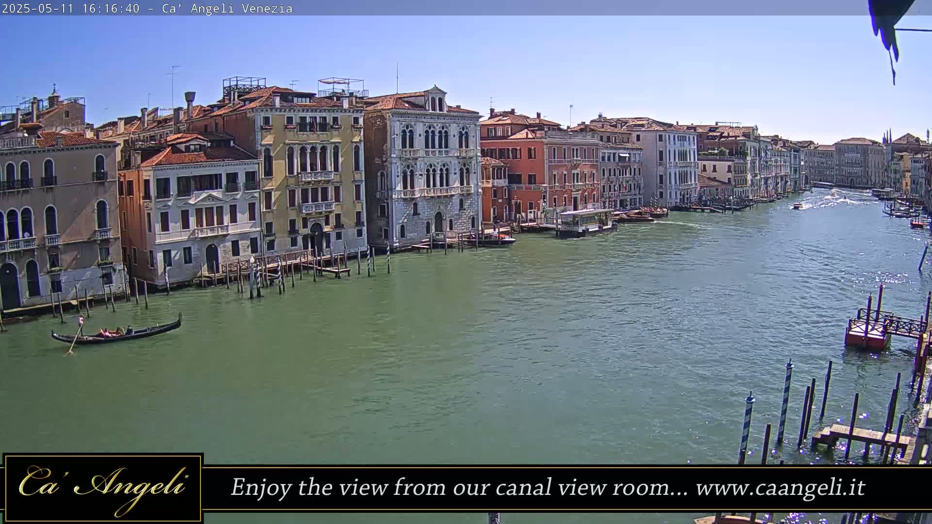 A gondola floats on a wide canal in Venice, Italy, under a clear blue sky, with numerous colorful buildings lining the waterway.