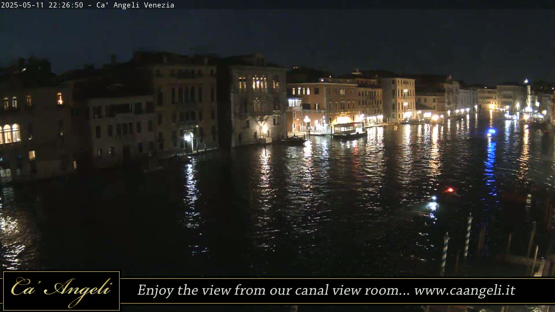 A nighttime view of a canal in Venice, with illuminated buildings lining the waterway and their lights reflected in the dark water.