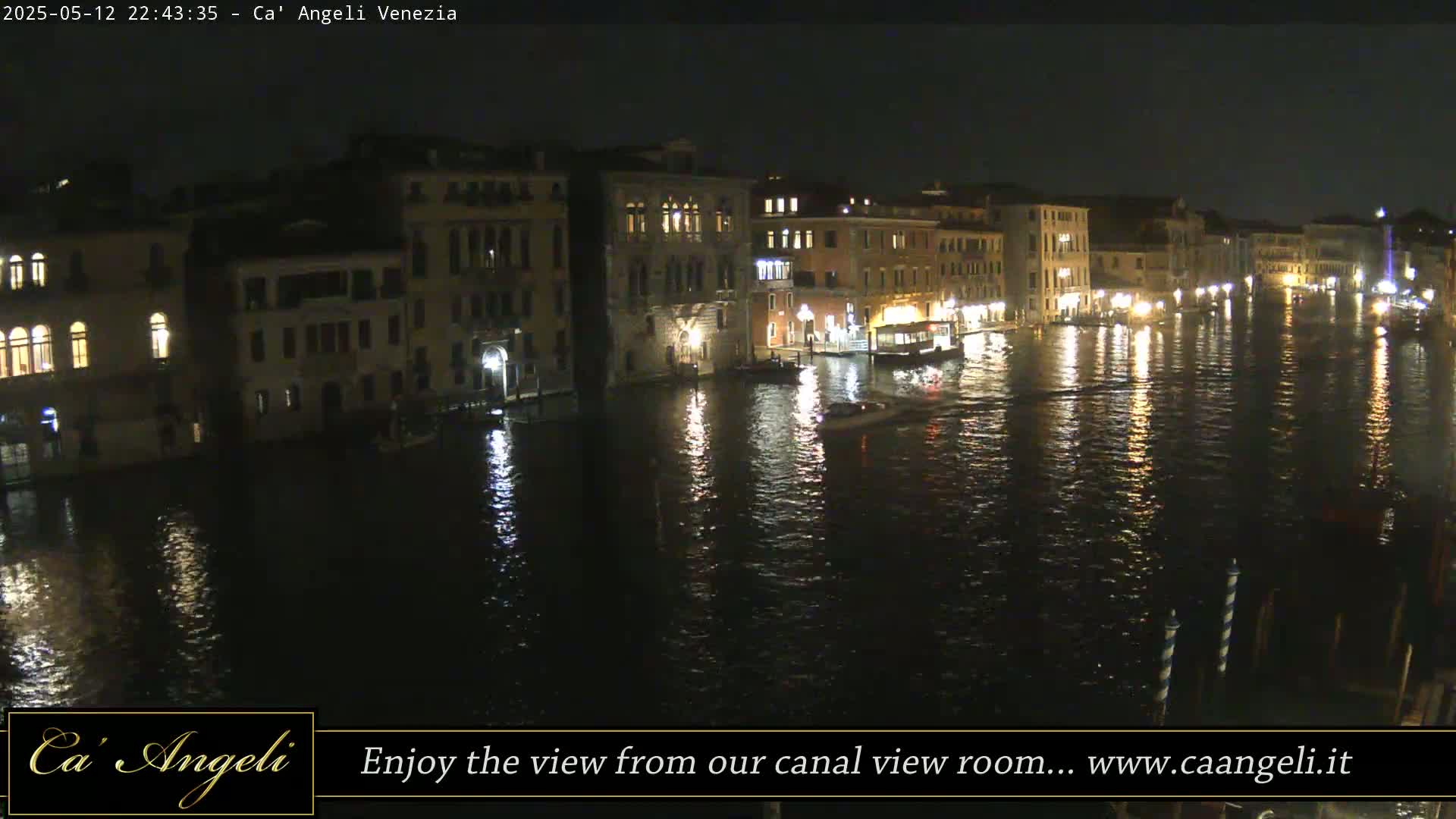 A nighttime view of a canal in Venice, with illuminated buildings lining the waterway and boats on the water.