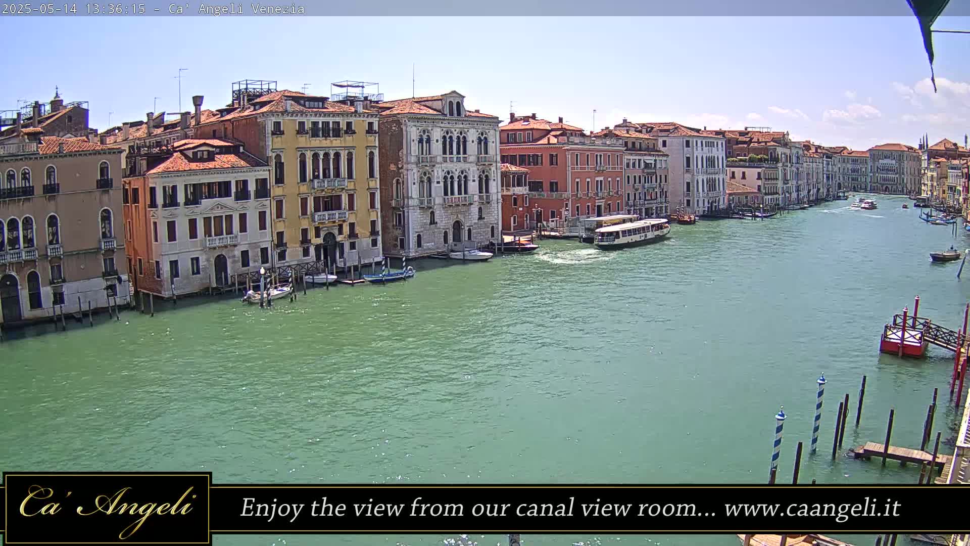 A waterway with several boats and colorful buildings lines its banks under a mostly sunny sky.