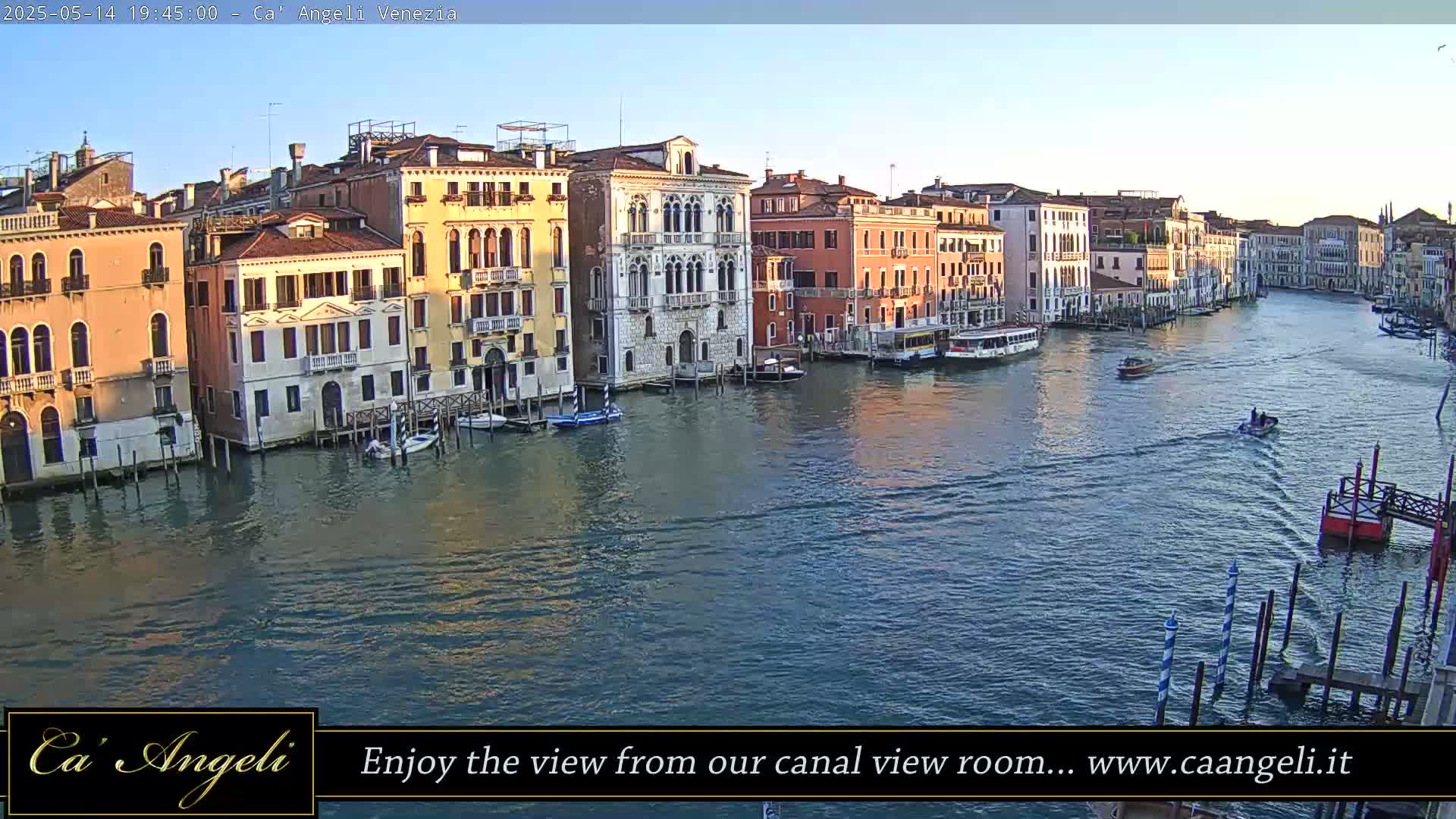 Under a clear sky, a wide canal in Venice is filled with boats, with colorful buildings lining its banks.