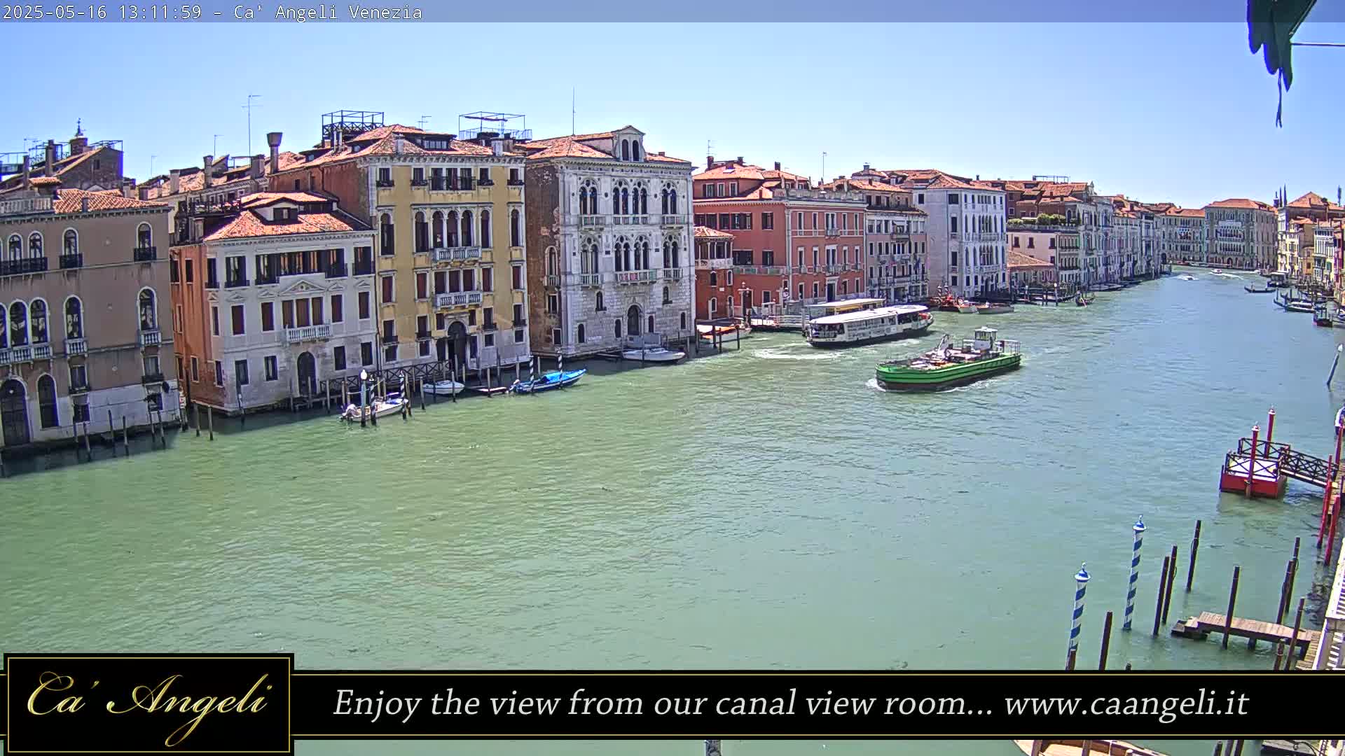 A sunny day in Venice shows a wide canal with colorful buildings lining the waterway, boats are visible on the water.