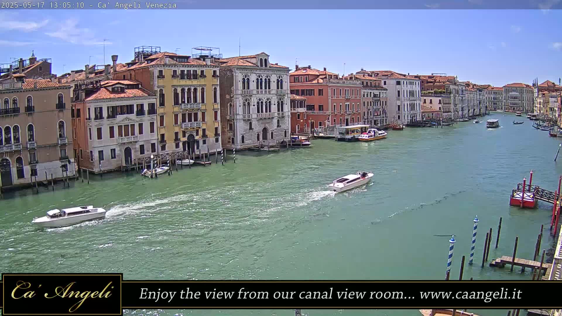 Under a sunny sky, several boats travel along a canal lined with colorful buildings in Venice.
