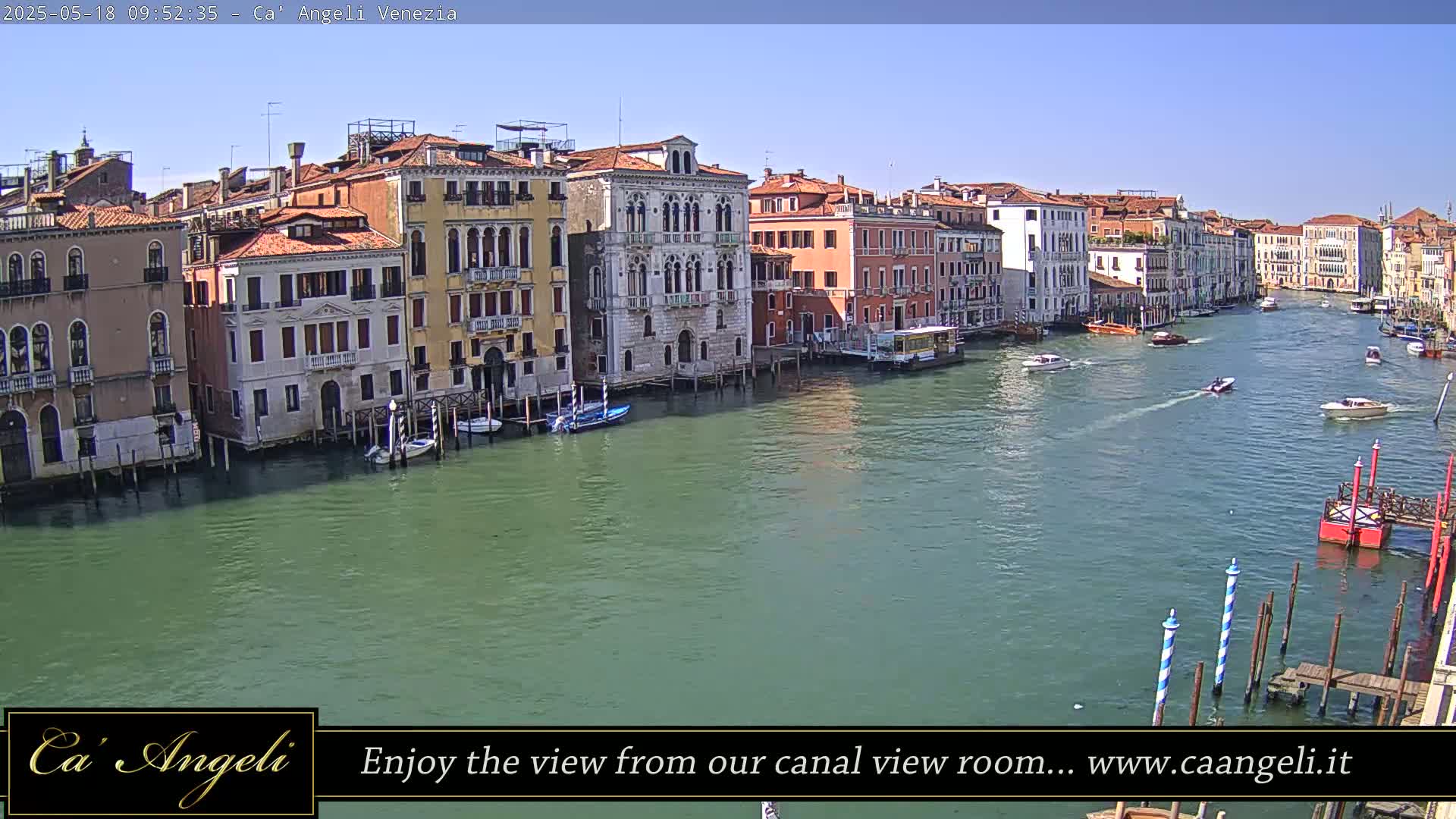 A sunny day in Venice shows several colorful buildings lining a canal with boats traveling on the water.