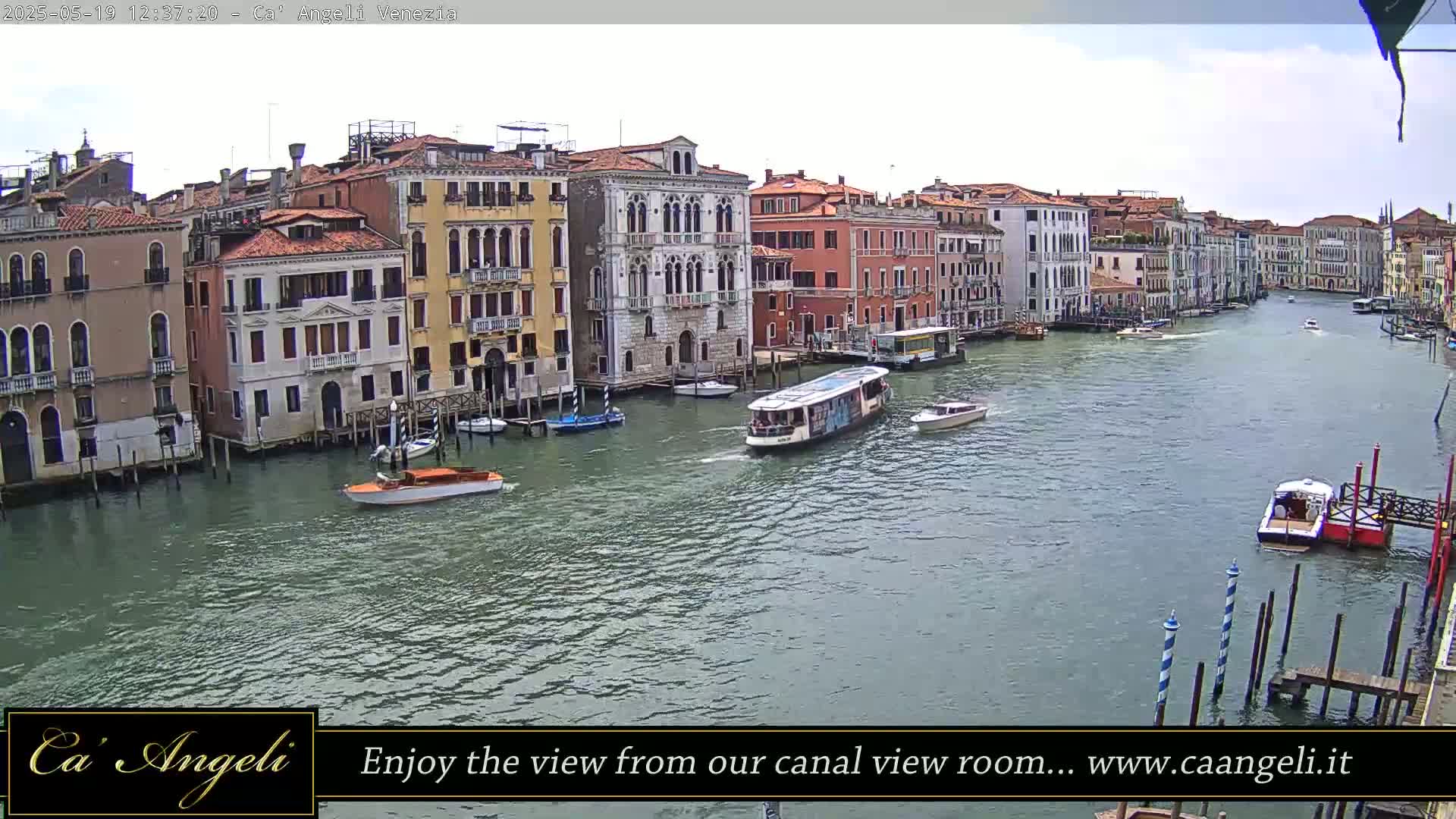 A wide canal in Venice, Italy, is filled with boats under a partly cloudy sky.