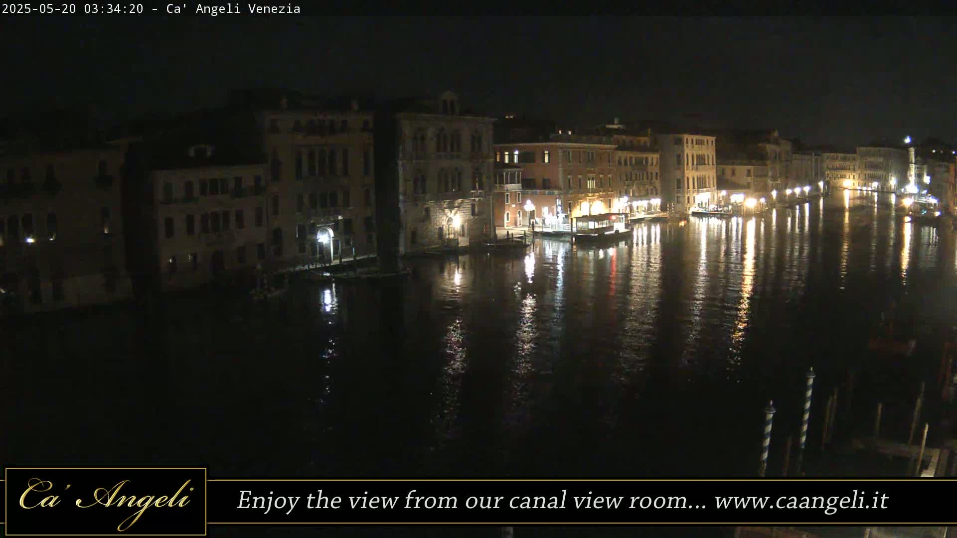 A nighttime view of a canal in Venice, Italy, shows illuminated buildings lining the waterway, their lights reflecting on the dark water.