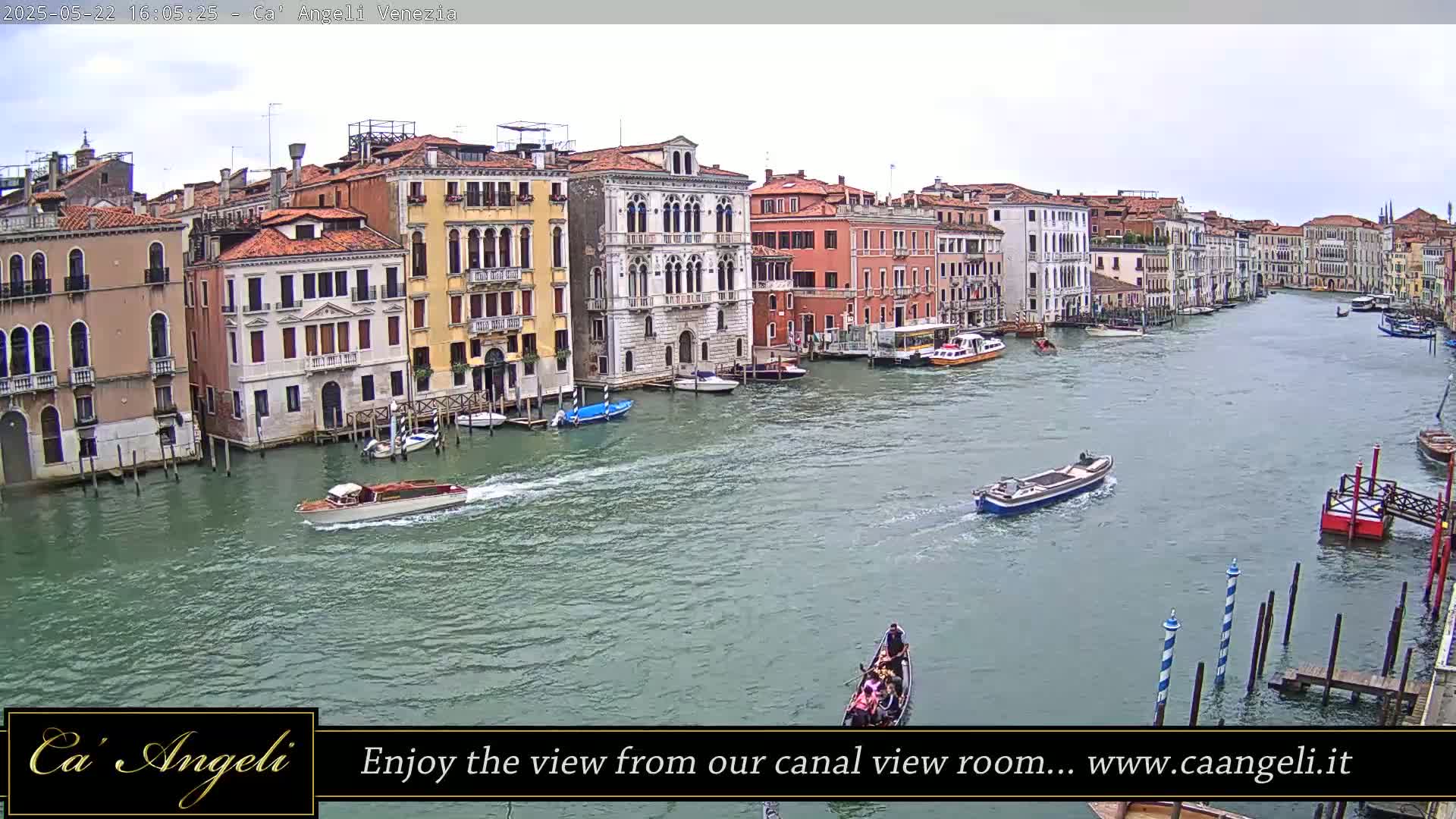 A wide shot of a canal in Venice on an overcast day, showing several boats and buildings lining the waterway.