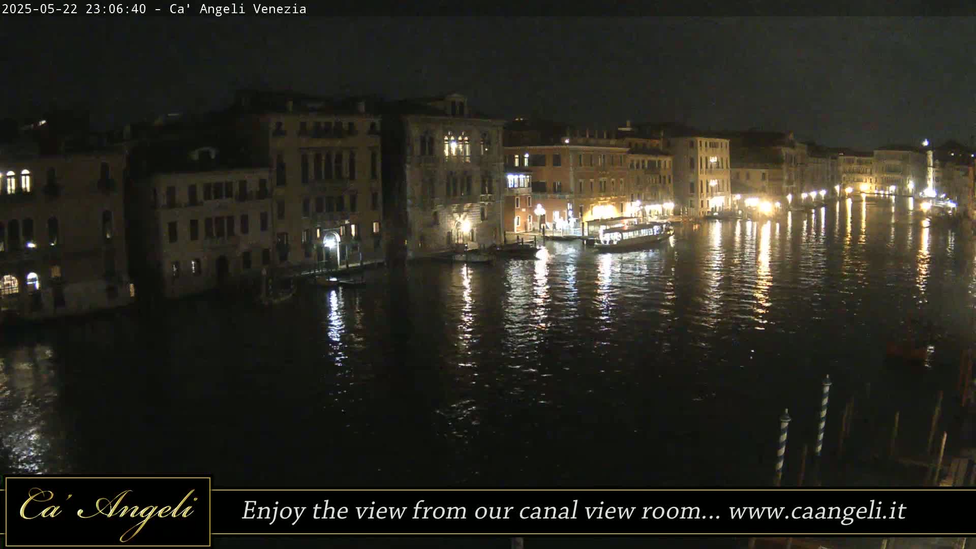 A nighttime view of a canal in Venice, with illuminated buildings lining the water's edge and boats moored along the banks.