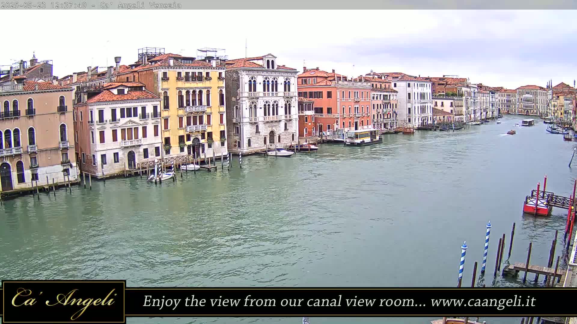 A wide shot of a calm canal in Venice, Italy, shows several colorful buildings lining the waterway under an overcast sky.
