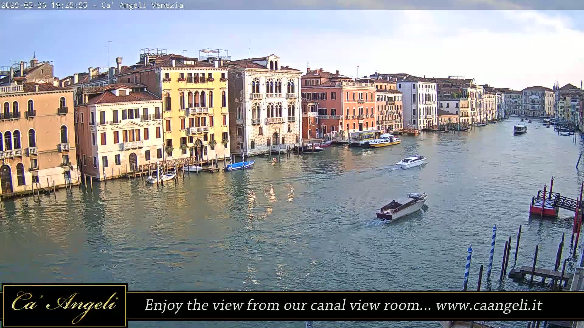 A wide shot of a Venetian canal at dusk, with colorful buildings lining the waterway and several boats moving along the water's surface.