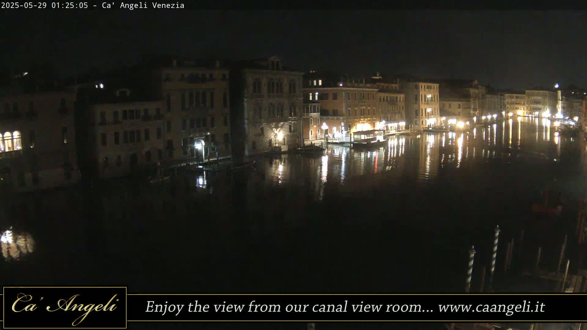 A nighttime view of a canal in Venice, Italy, shows illuminated buildings reflected in the dark water.