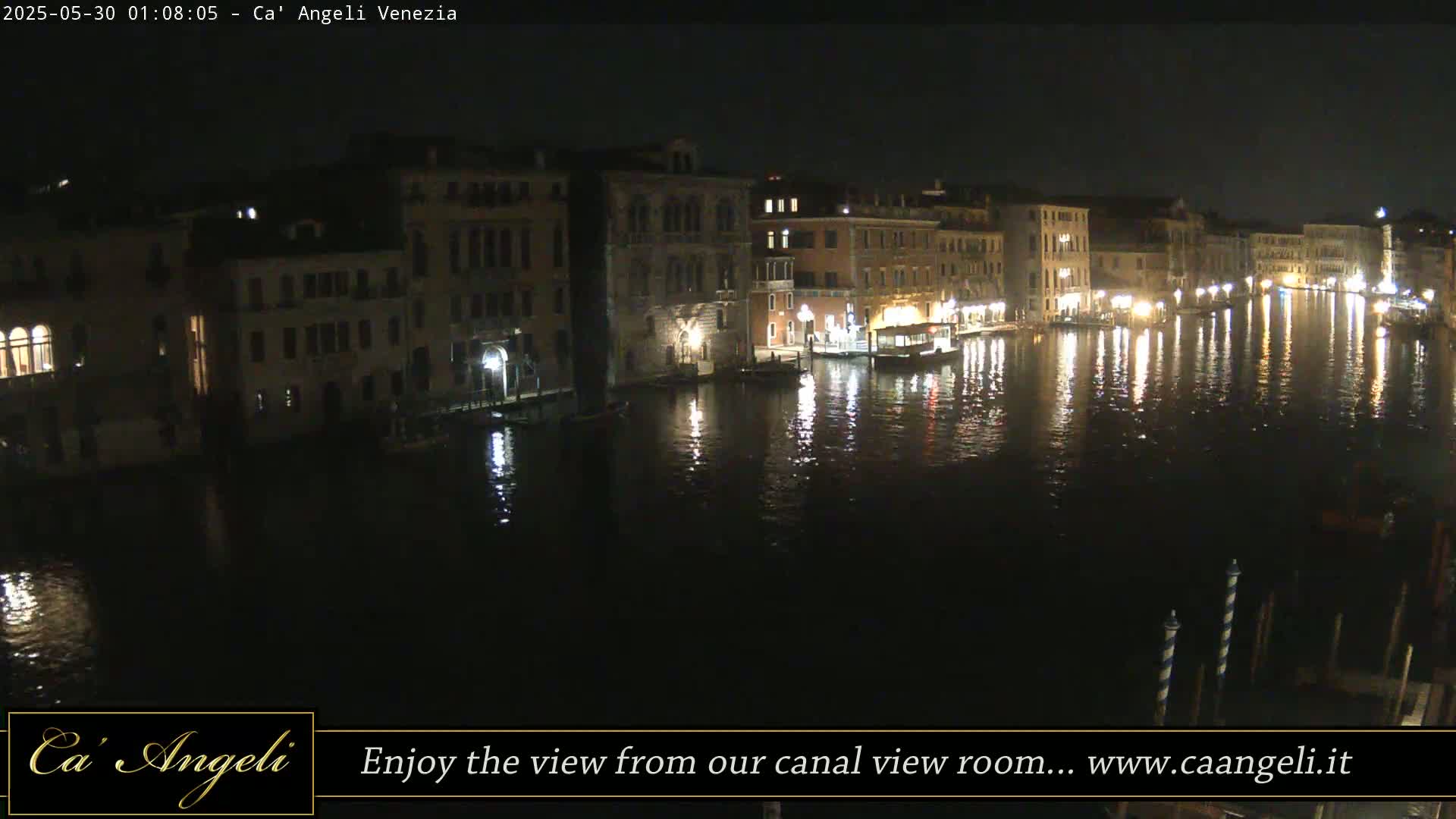 A nighttime view of a canal in Venice, Italy, with illuminated buildings lining the waterway and their lights reflecting on the calm water.