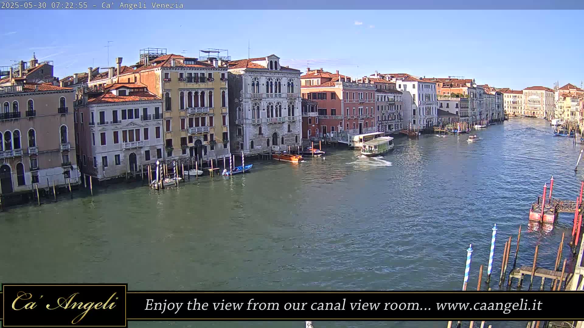 A wide canal in Venice, Italy, is shown on a sunny day with several boats and historic buildings lining its banks.
