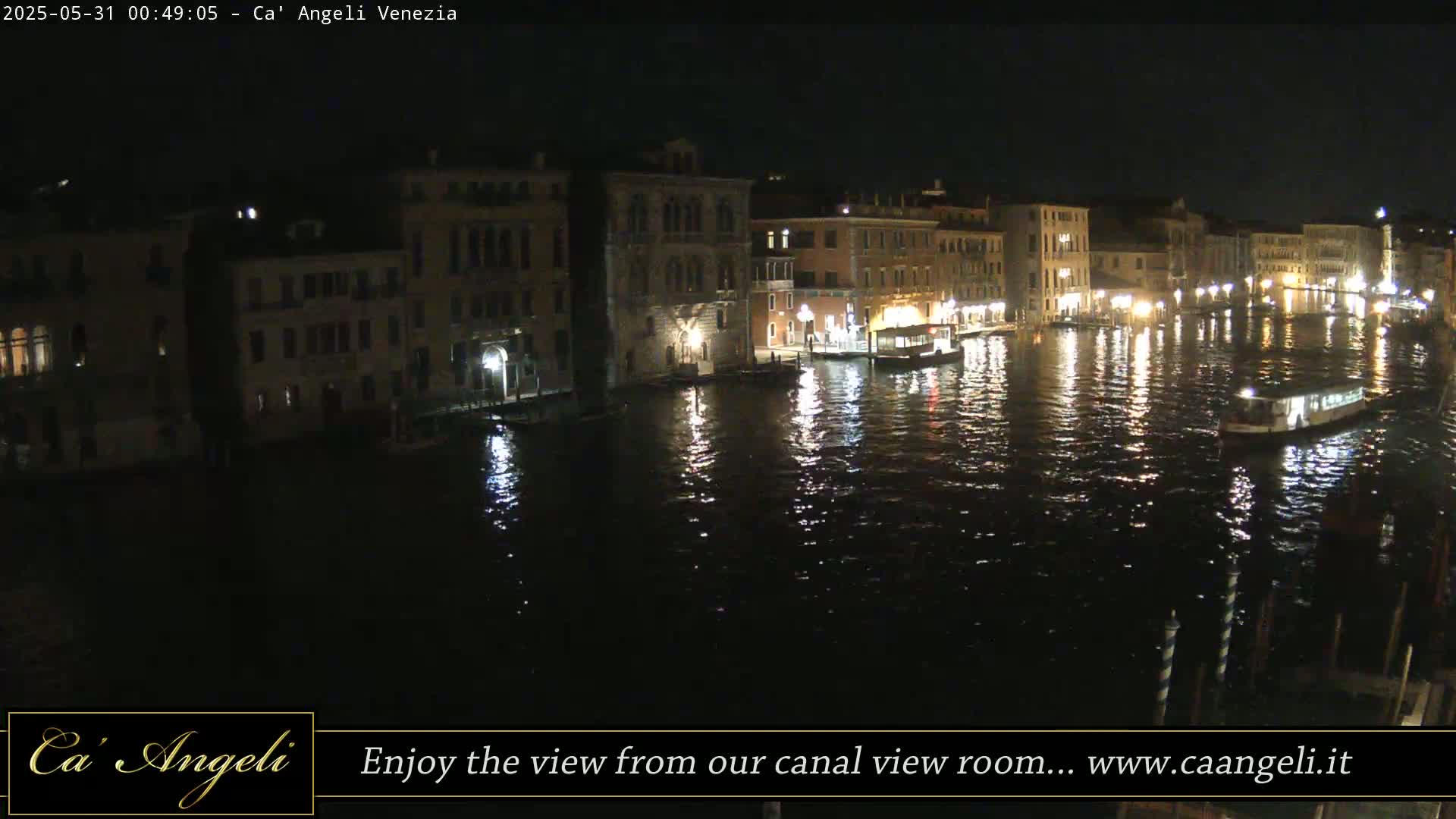 A nighttime view of a canal in Venice, Italy, shows several buildings lit along the waterway with boats on the dark water.