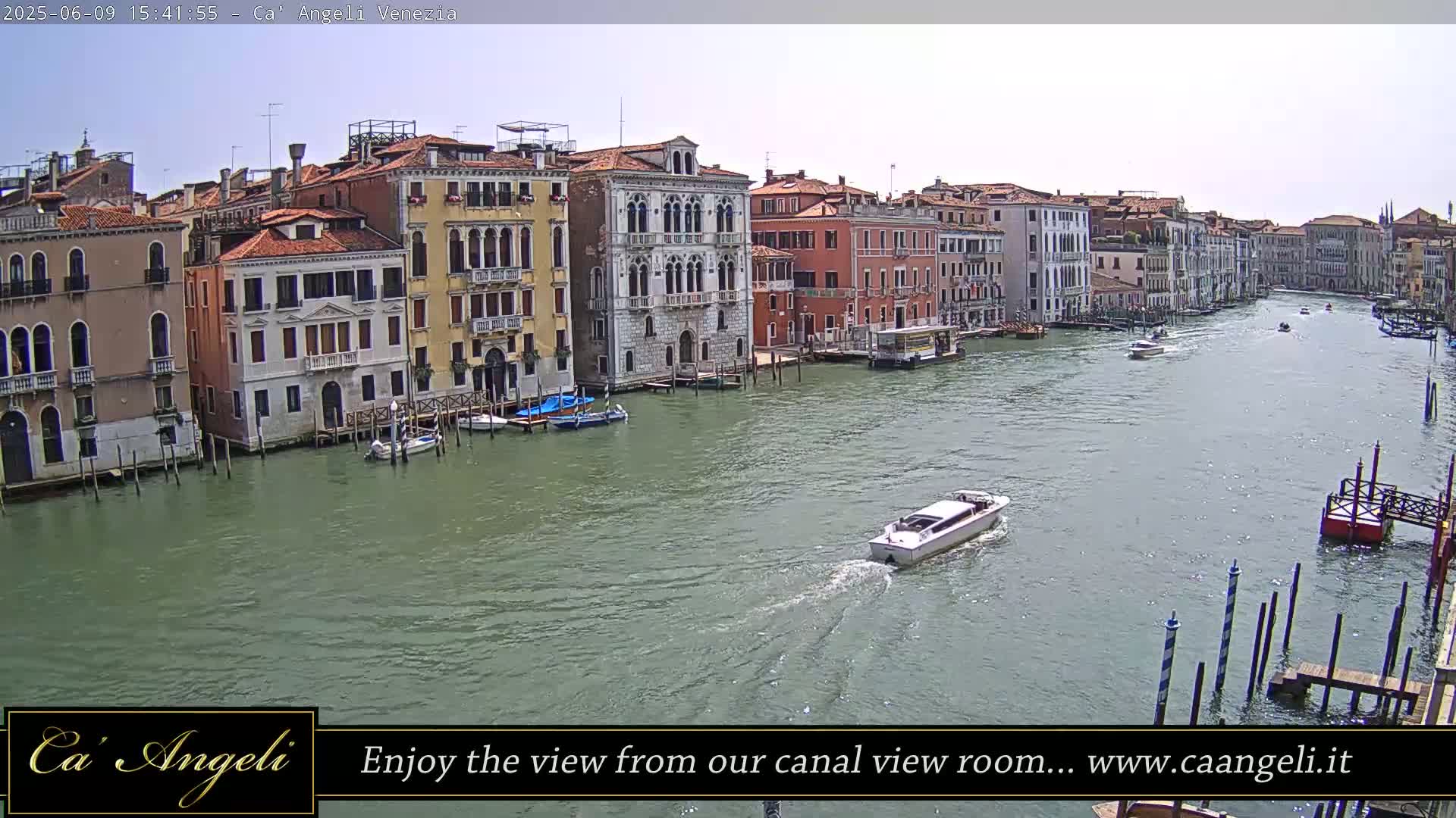 A sunny day in Venice shows a canal with several boats and numerous buildings lining the waterway.