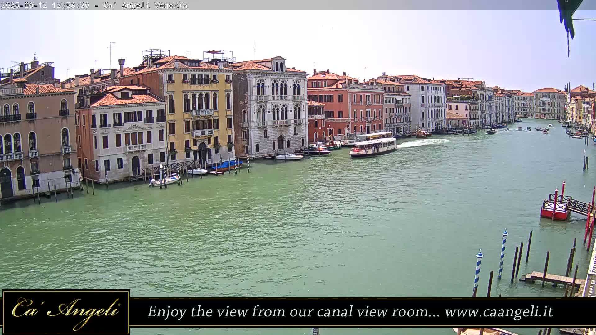 A sunny day reveals a Venetian canal with colorful buildings lining its banks, boats moored alongside, and a water bus moving down the waterway.
