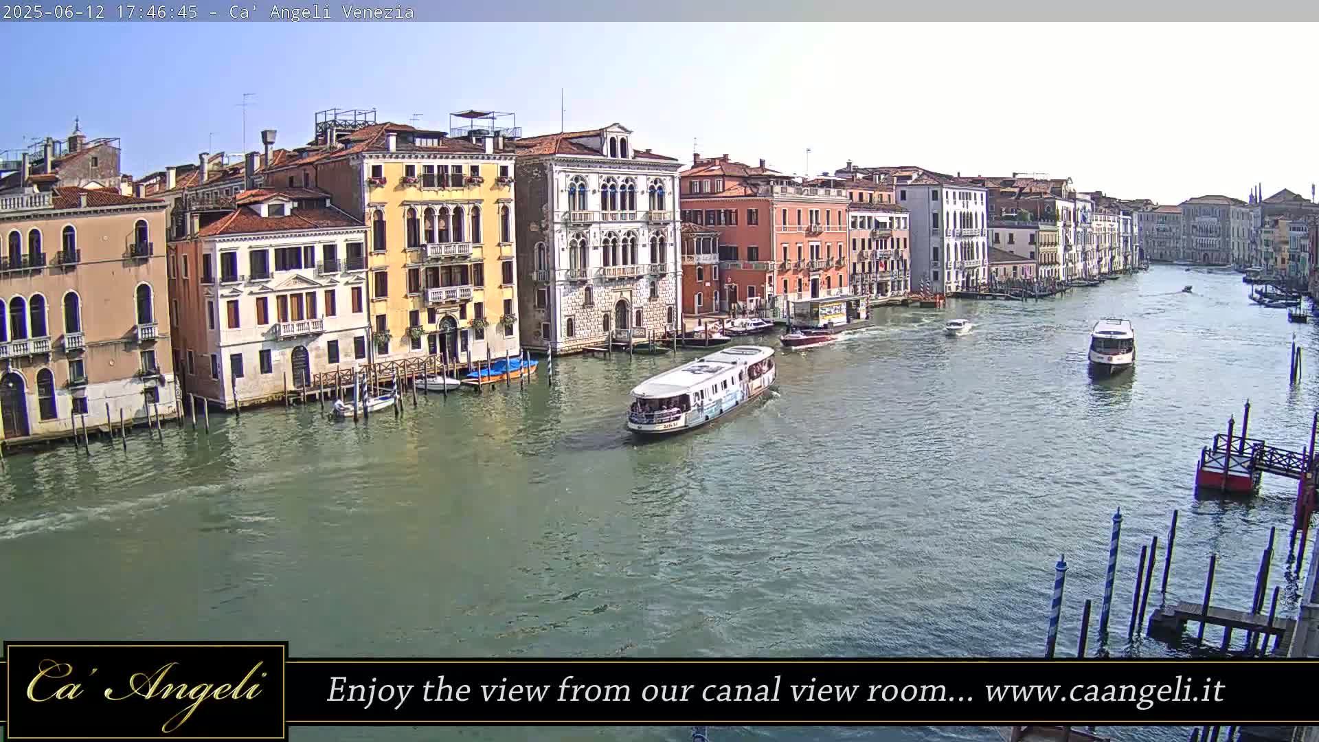 A sunny day in Venice shows a wide canal with several boats and colorful buildings lining the waterway.