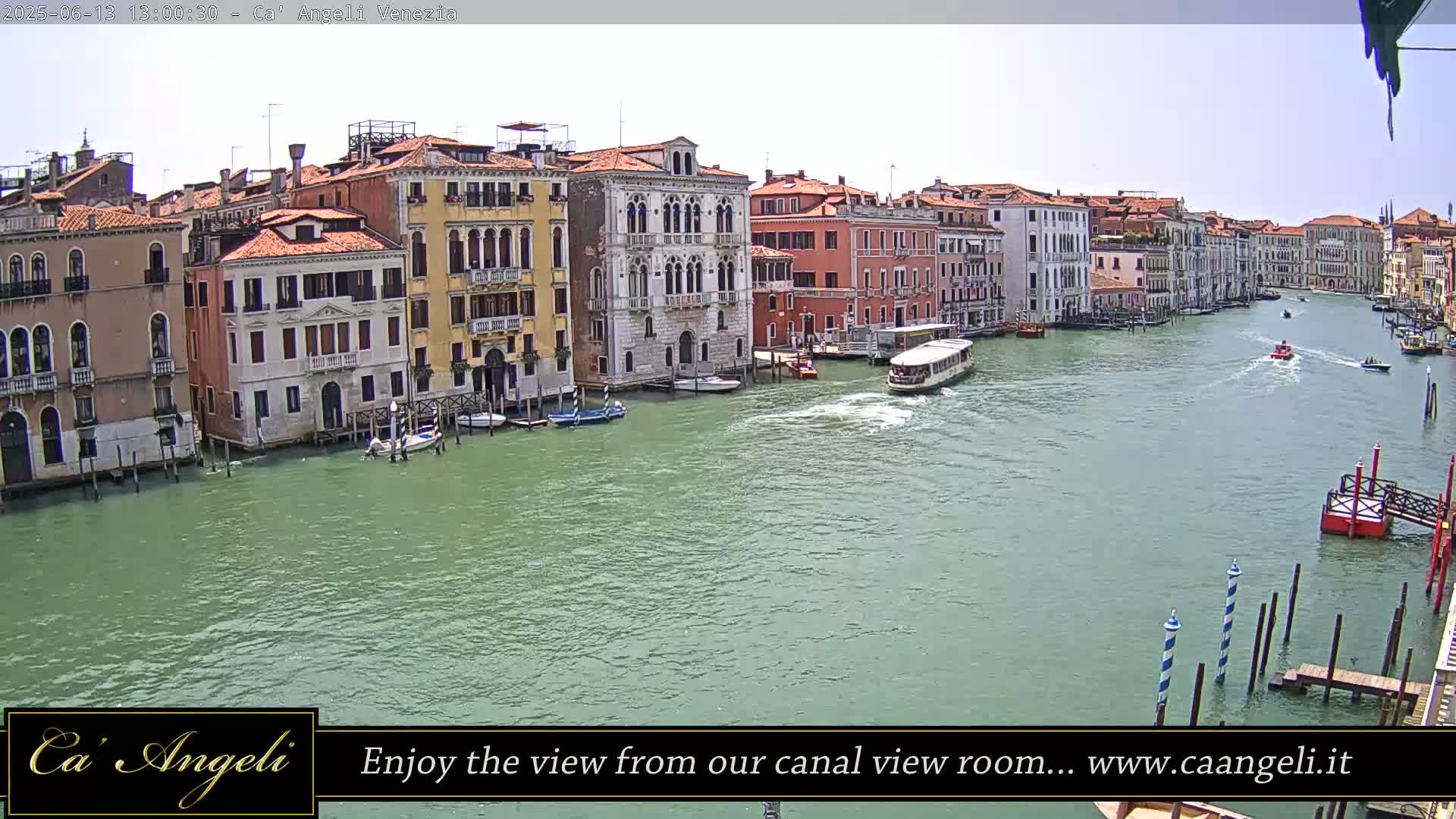 A sunny day in Venice shows a wide canal with boats and numerous buildings lining its banks.