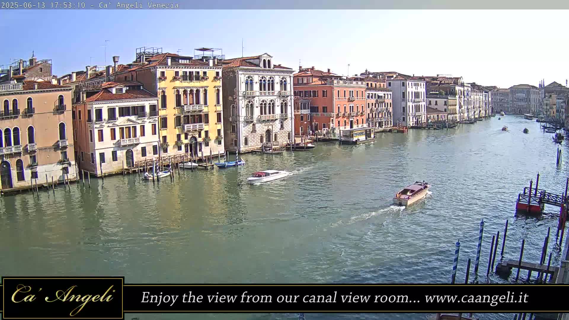 A sunny day in Venice shows several boats on a canal, lined with tall, colorful buildings.