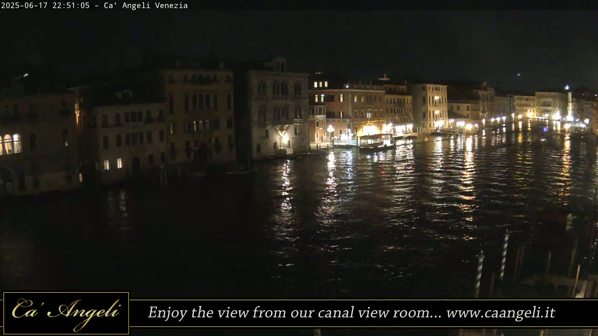 A nighttime view of a canal in Venice, Italy, showing illuminated buildings reflected in the dark water.
