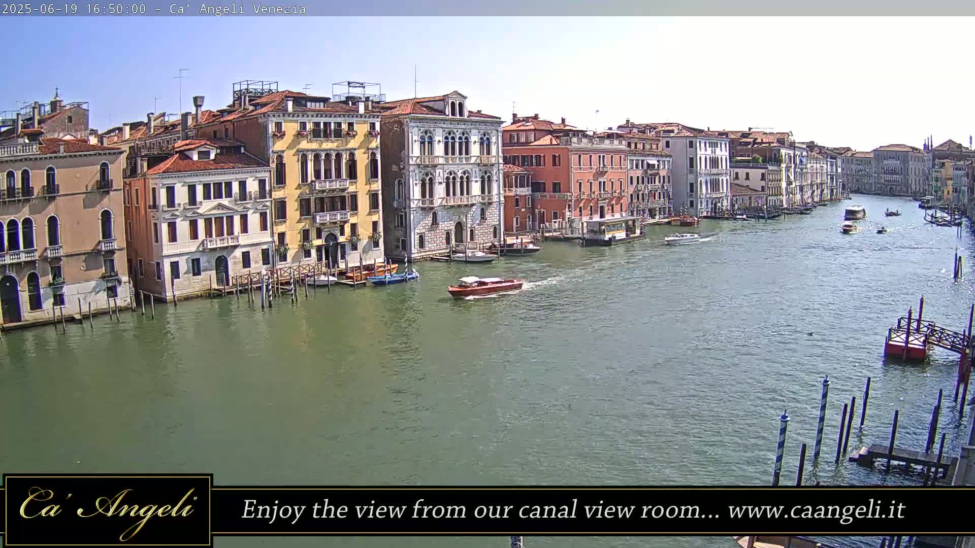 A sunny day shows a wide canal in Venice, Italy, lined with colorful buildings, with several boats traveling on the water.