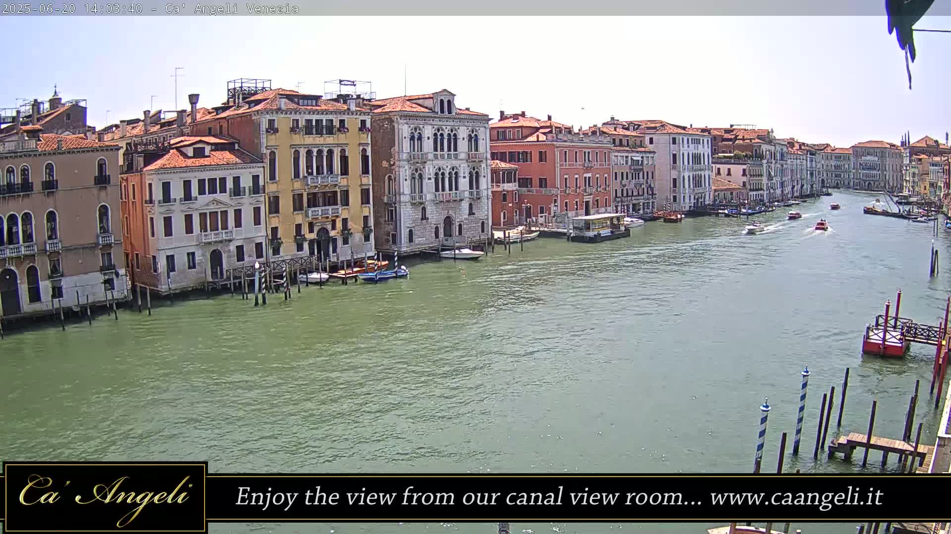 A wide shot of a canal in Venice, Italy on a sunny day, shows numerous buildings lining the waterway with boats traveling along it.