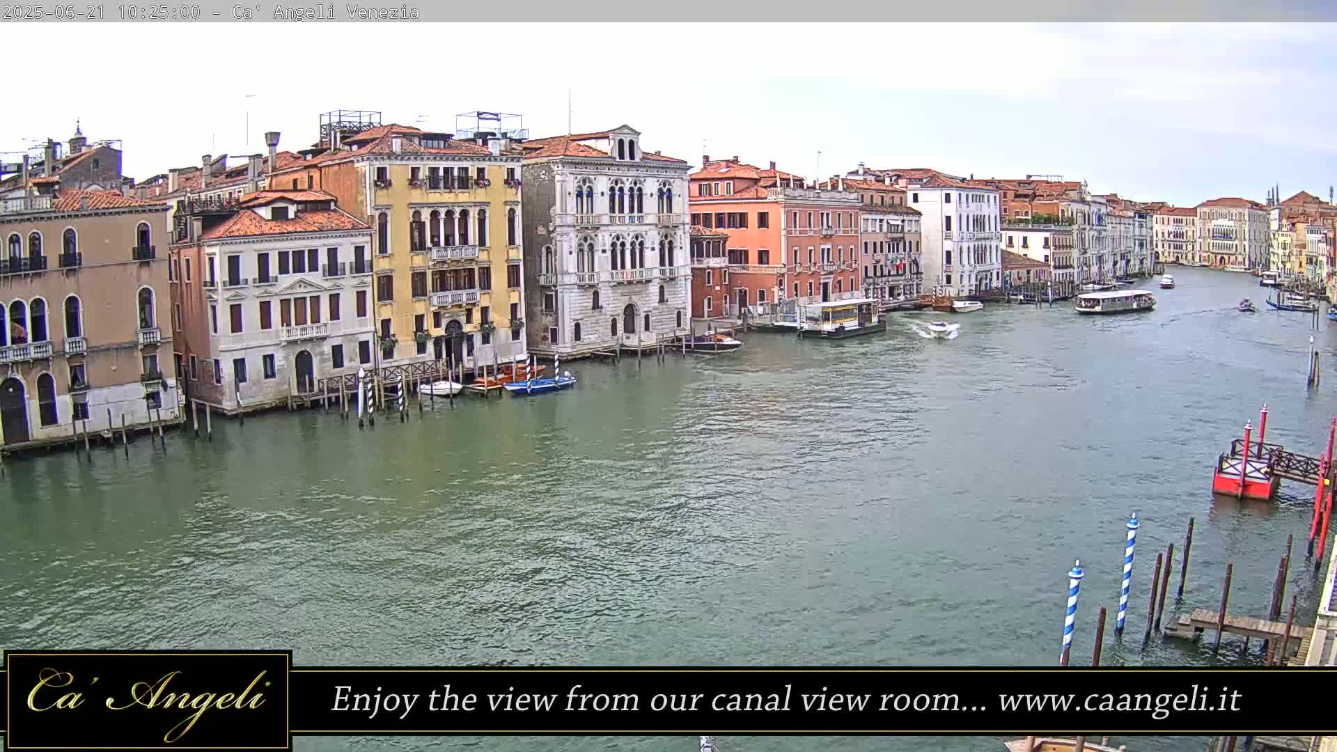 A wide shot of a canal in Venice, Italy, shows several colorful buildings along the water's edge with boats on the calm water under a mostly clear sky.