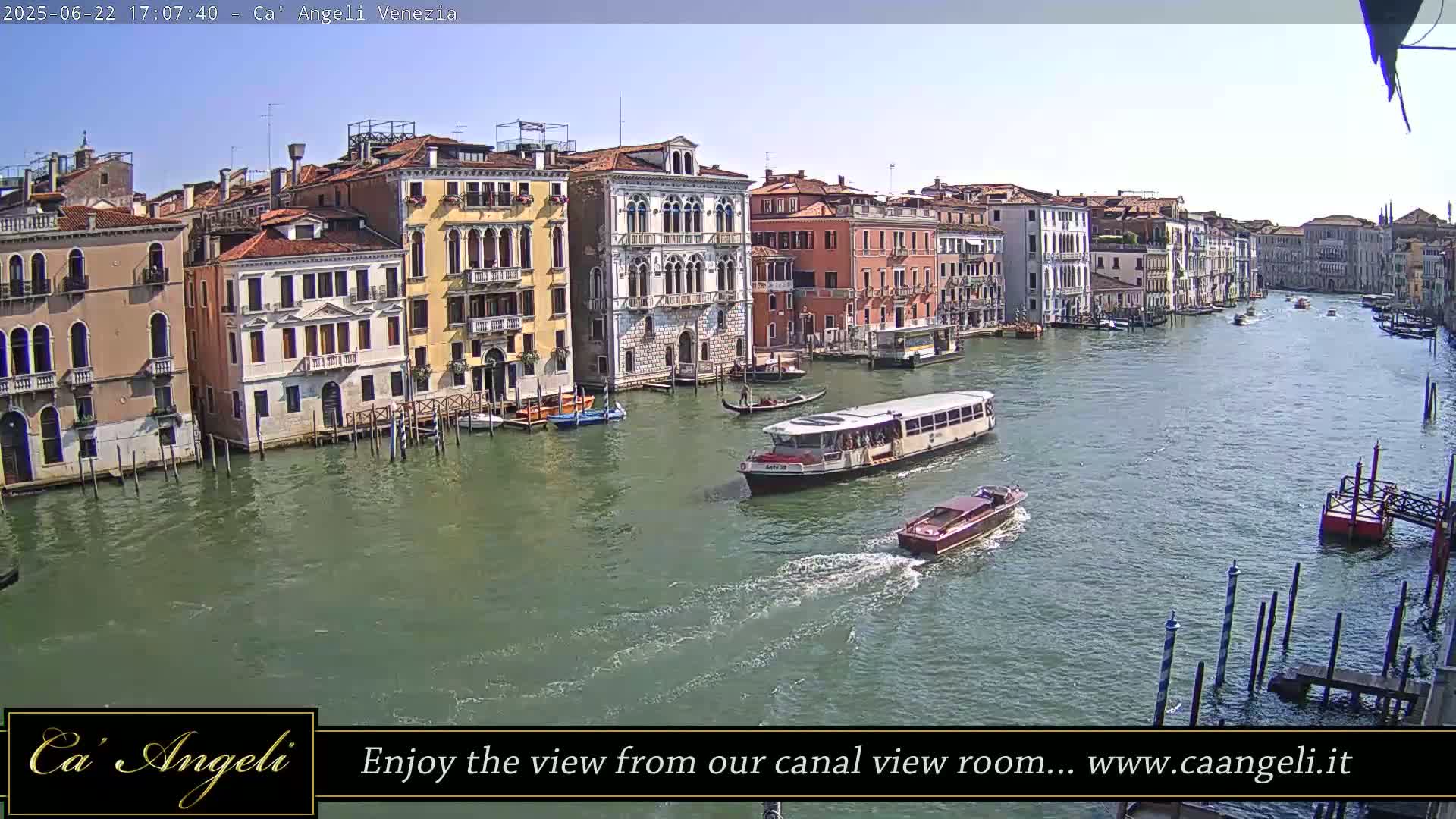 A sunny day shows a wide canal in Venice, Italy, with numerous boats and colorful buildings lining the waterway.