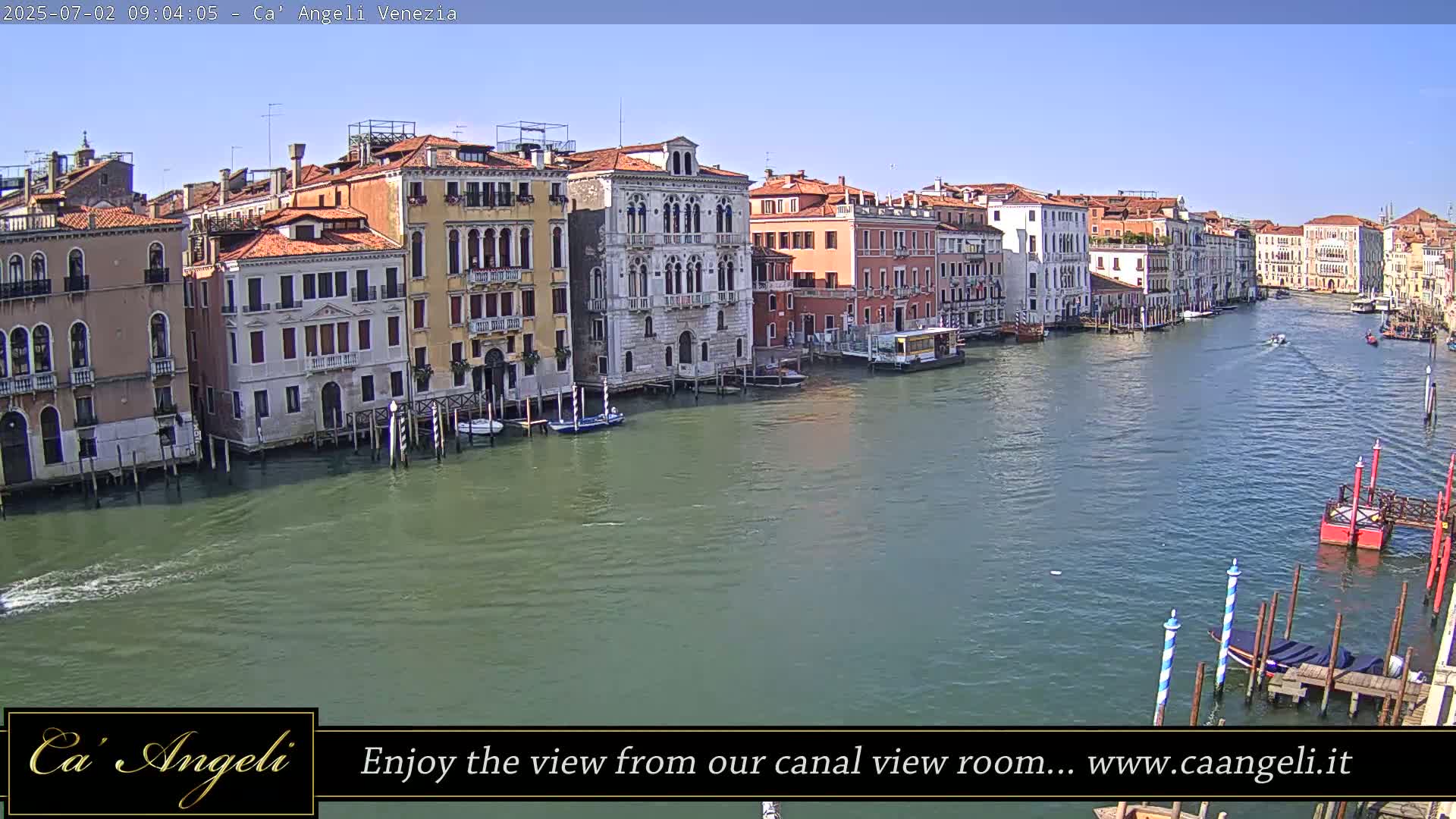 A sunny day in Venice shows a wide canal lined with colorful buildings, boats, and mooring posts.