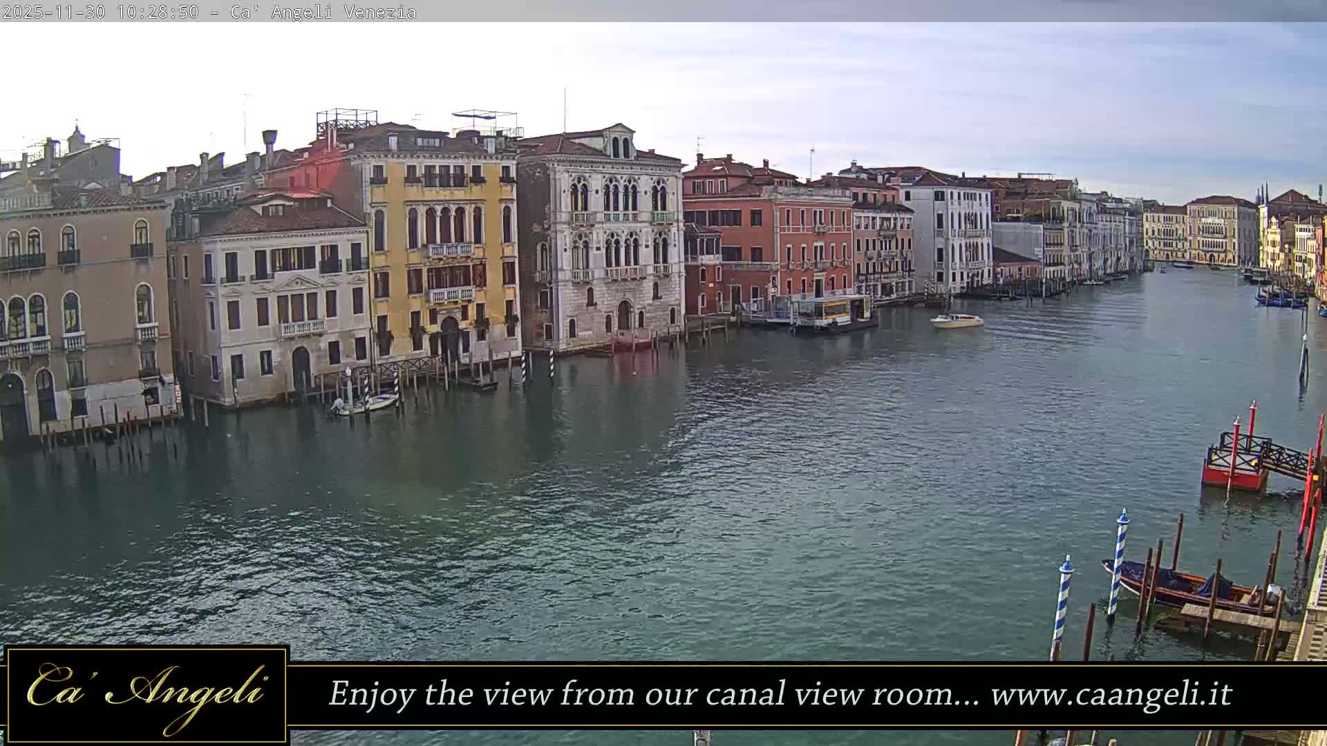 The Grand Canal in Venice is seen winding through historic buildings under an overcast sky, with various boats navigating the calm waters.