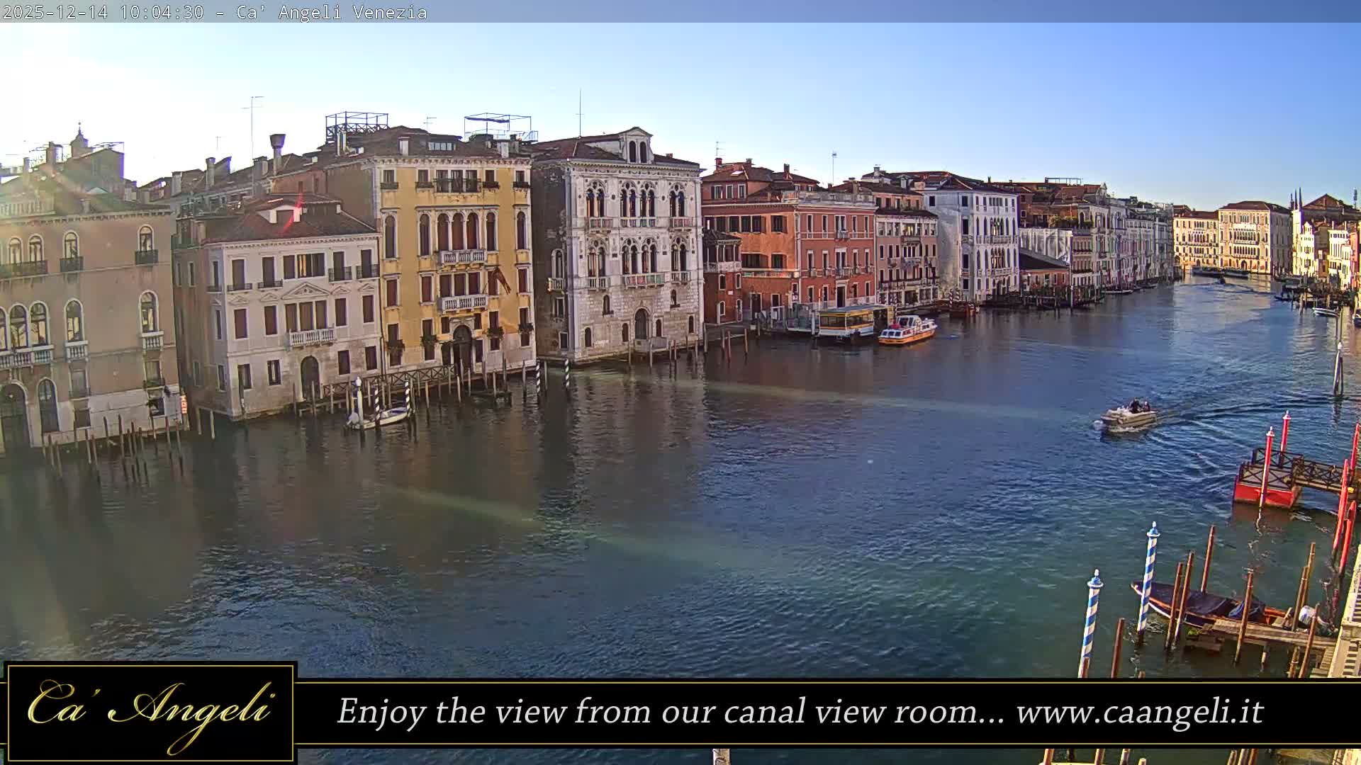 A busy Venetian canal, lined with colorful historic buildings, is traversed by numerous boats under a bright, overcast sky.