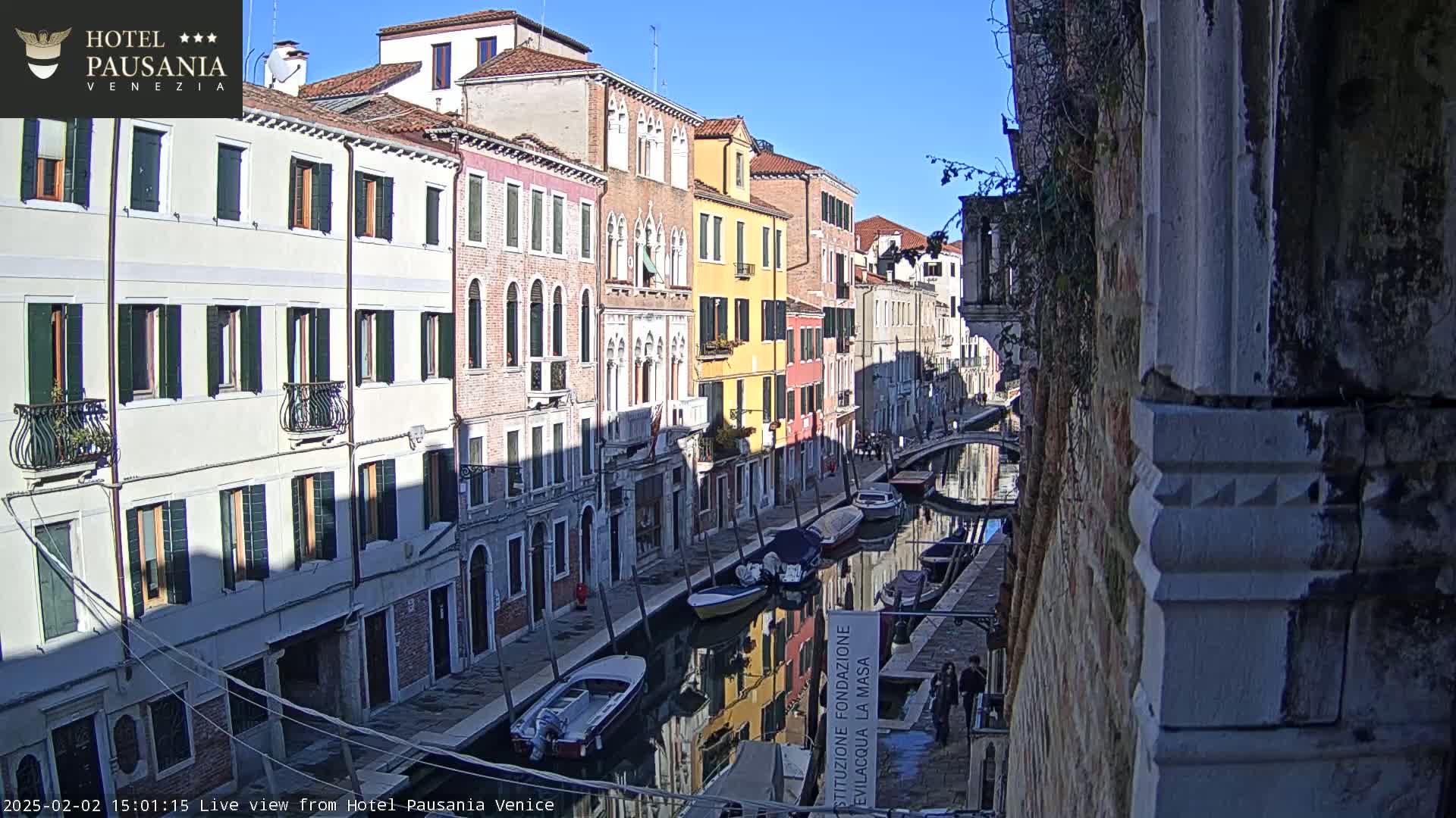 A sunny view of a narrow Venetian canal lined with colorful buildings and several small boats.