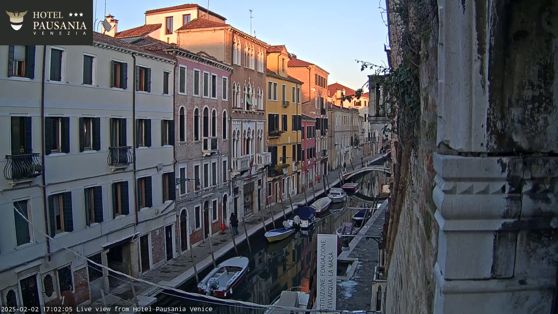 A narrow Venetian canal at sunset, lined with colorful buildings and several moored boats.