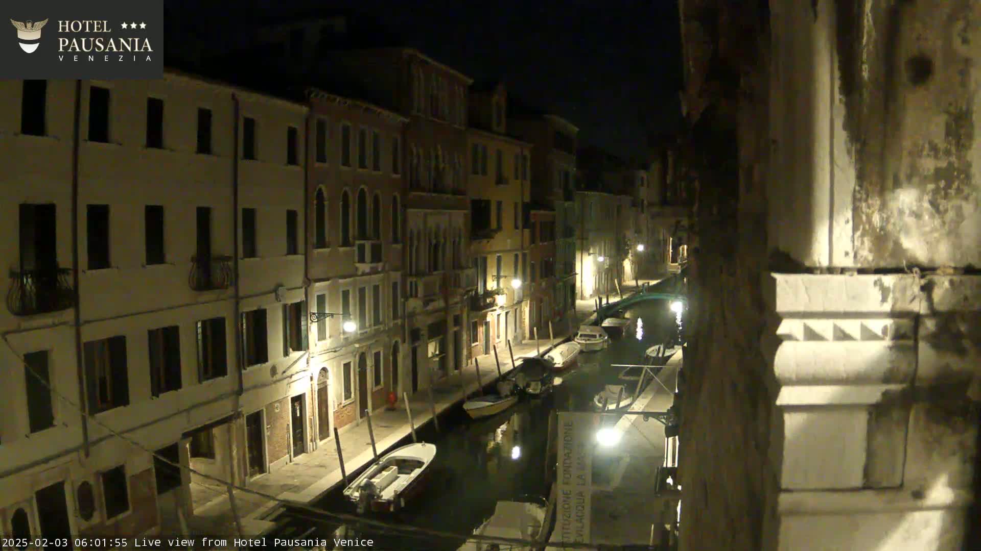 Several boats are moored along a canal at night, flanked by illuminated buildings.