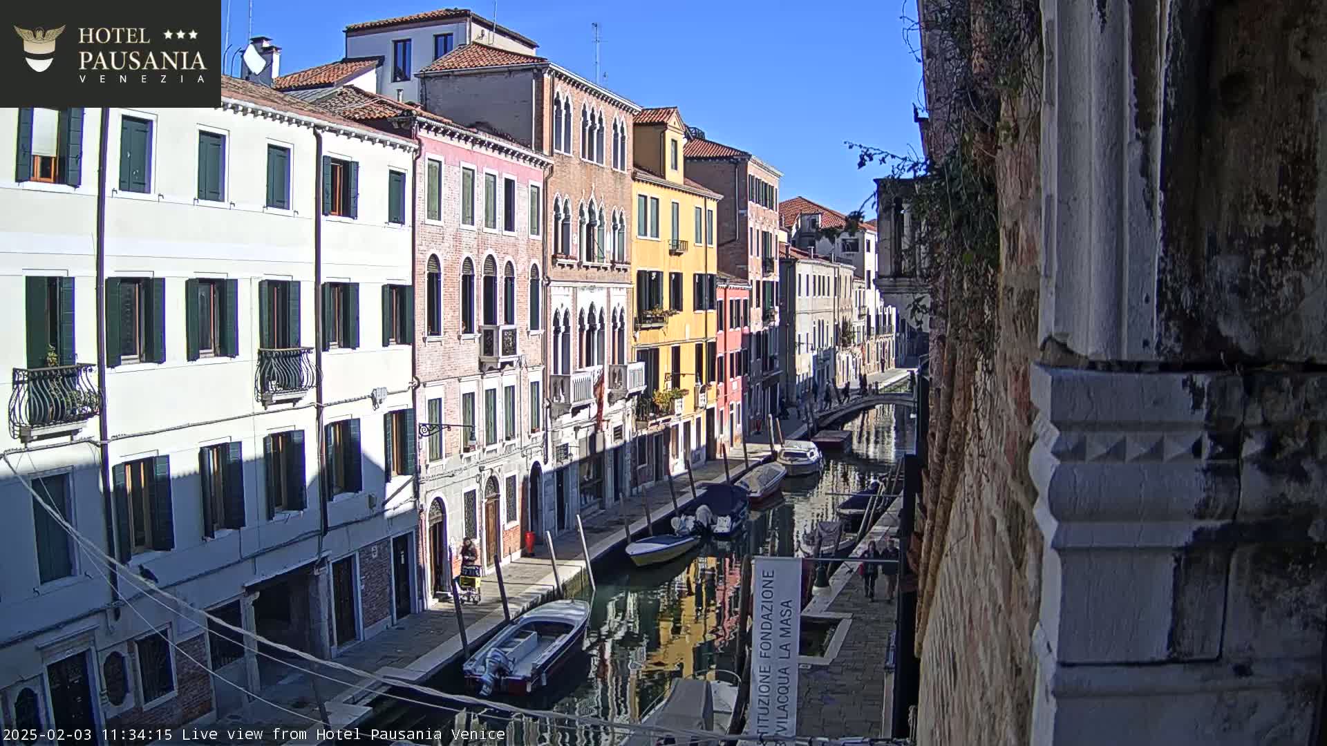 A sunny day in Venice, showing a canal lined with colorful buildings and several boats.