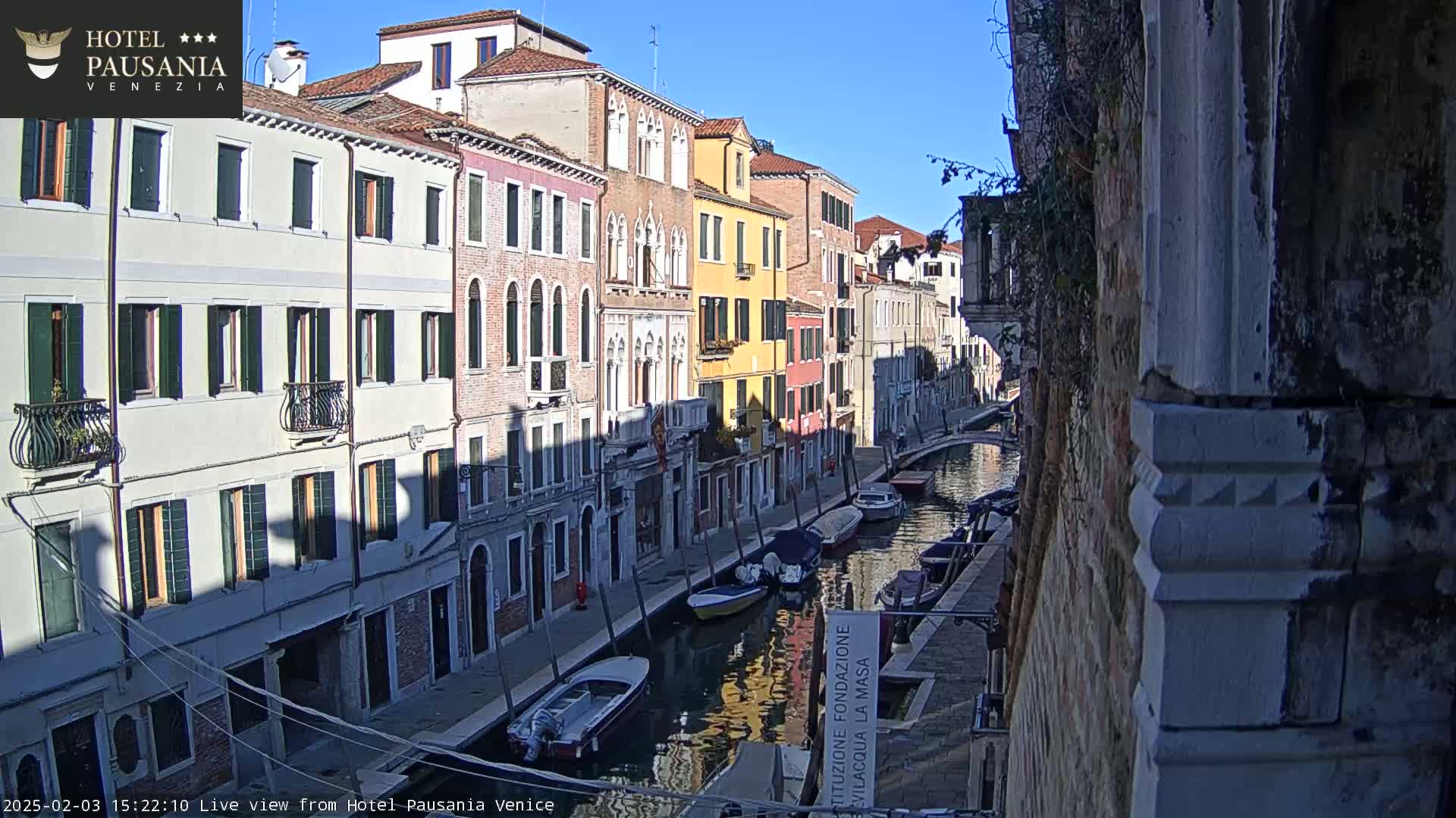 A sunny day in Venice shows several colorful buildings lining a canal where several small boats are moored.