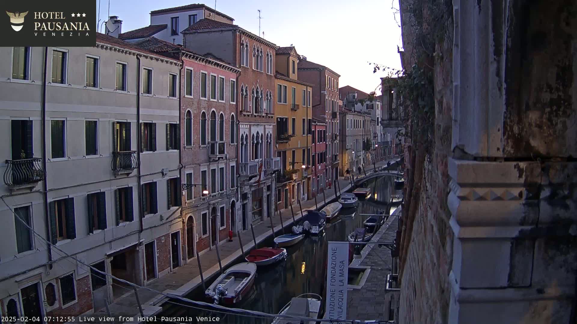 A narrow Venetian canal at dawn, lined with colorful buildings and several moored boats.