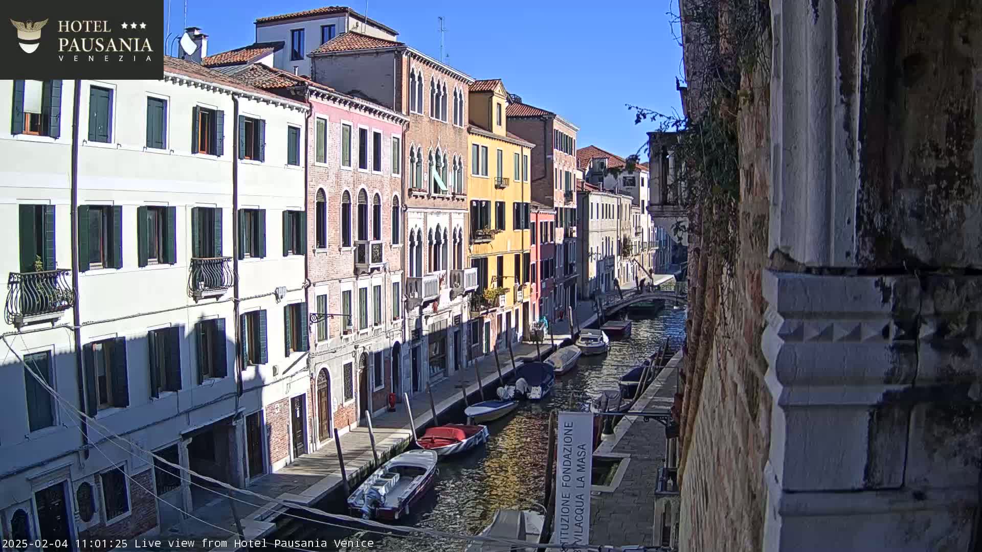 A sunny day in Venice shows several colorful buildings lining a canal with moored boats.