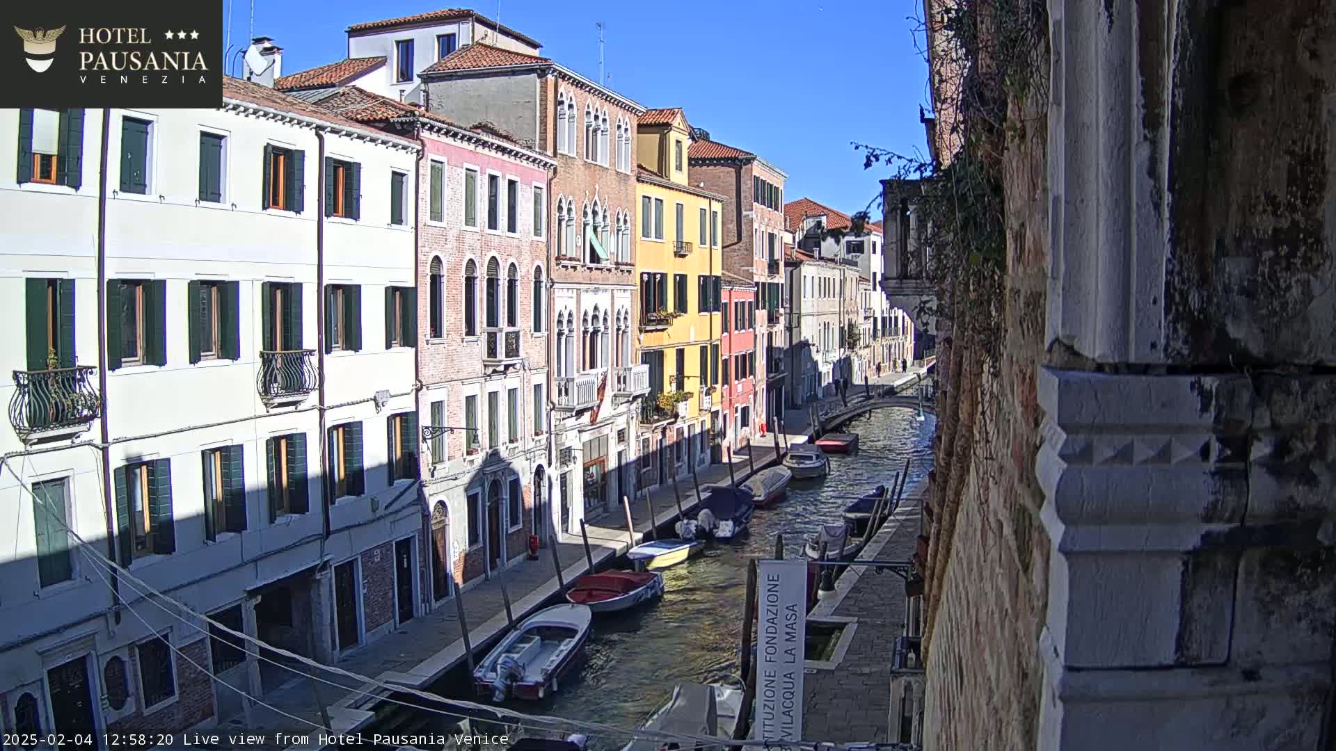 A sunny day in Venice shows colorful buildings lining a canal where several boats are moored.