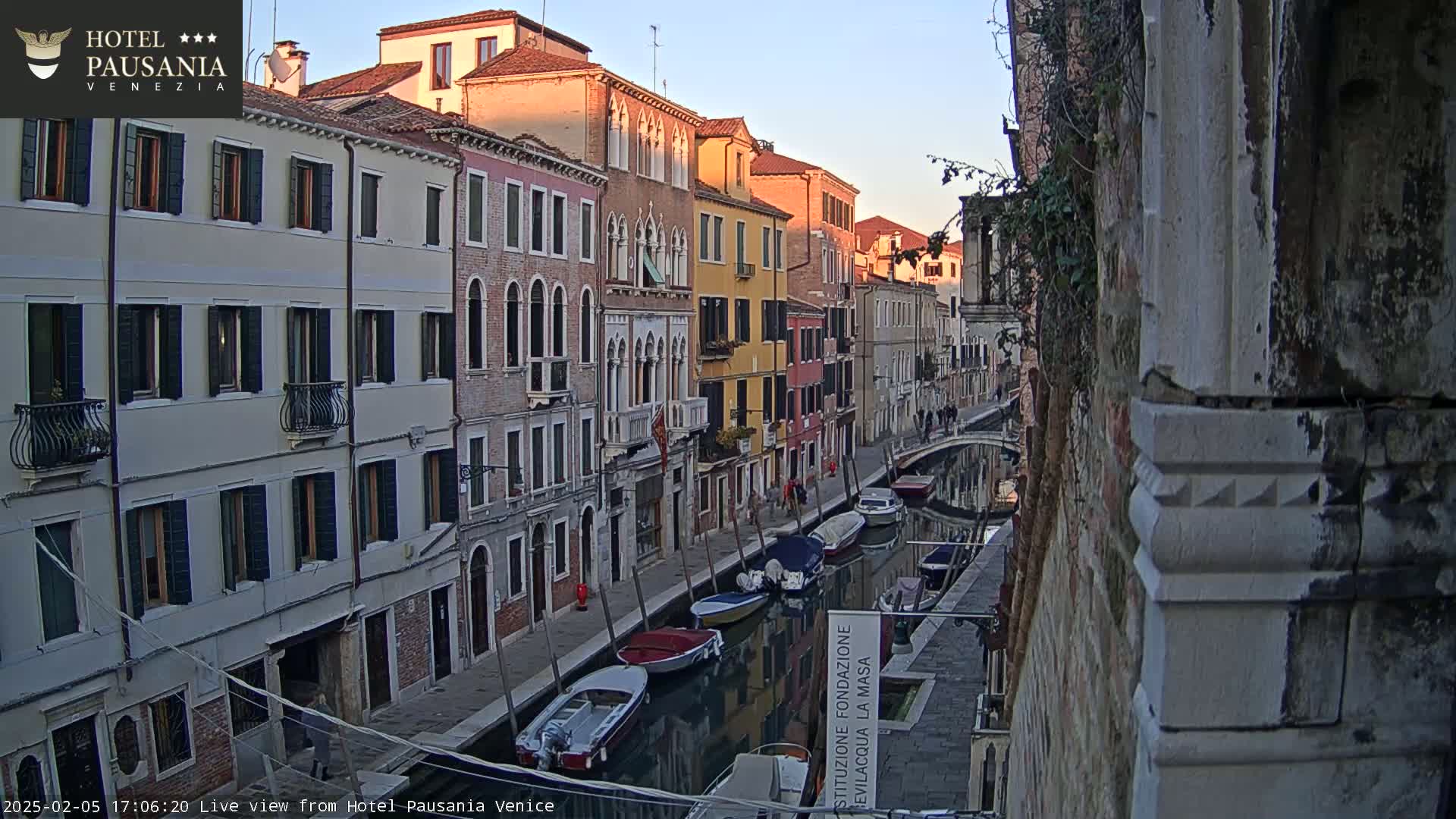 A calm canal in Venice at sunset, lined with colorful buildings and several moored boats.