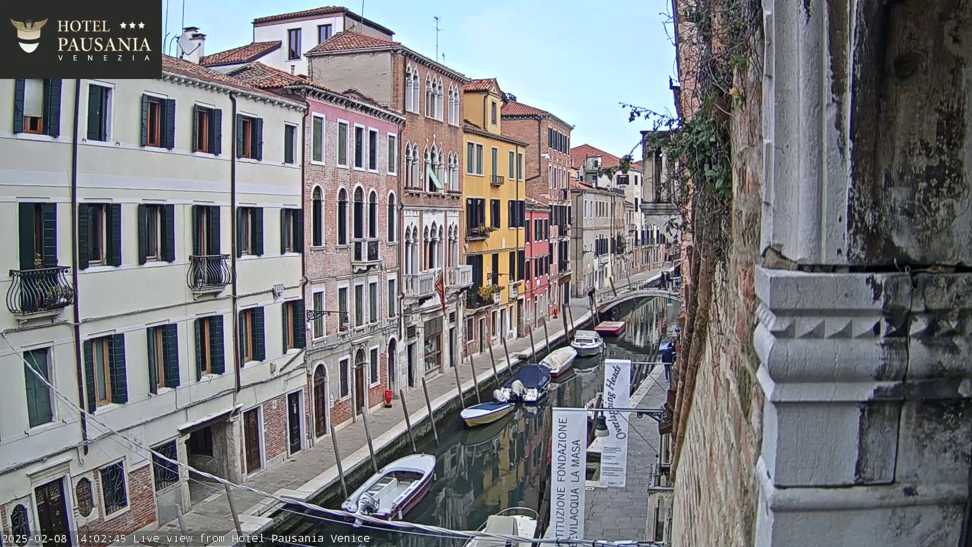 A narrow canal in Venice, Italy, is lined with colorful, closely situated buildings under a mostly clear sky.