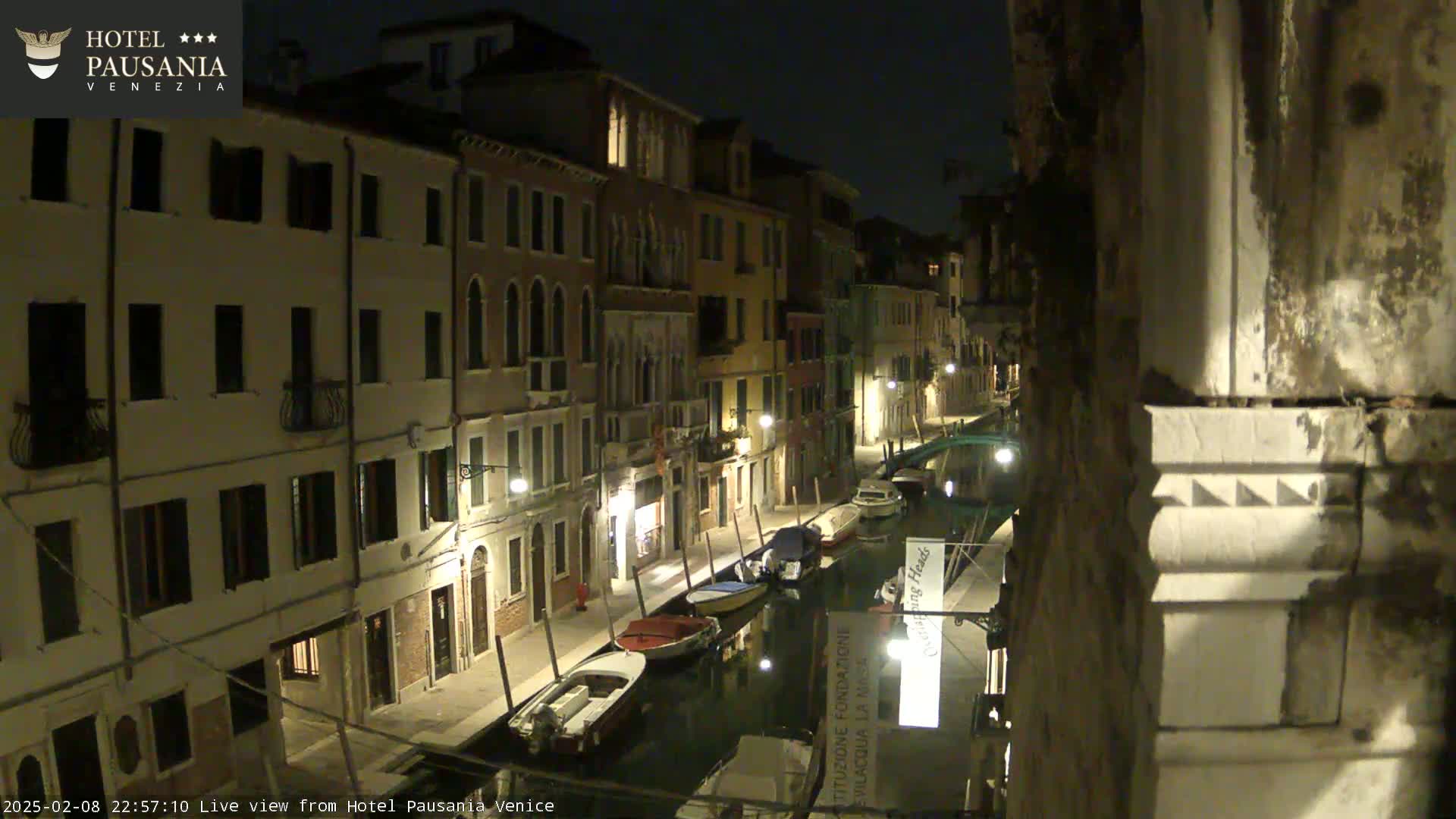 A nighttime view of a canal in Venice, showing several boats moored along the waterway and buildings illuminated by streetlights.
