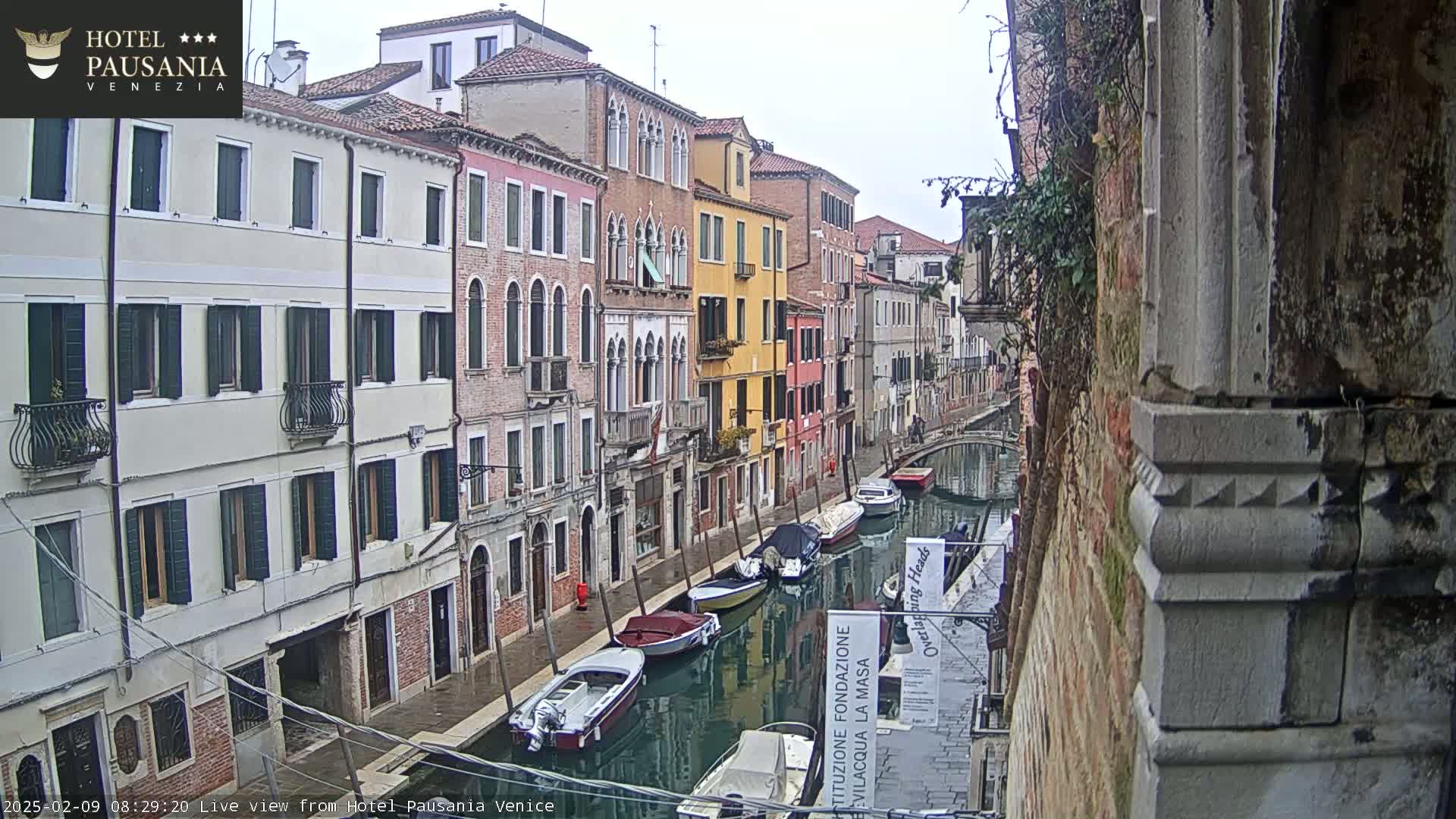 A narrow canal in Venice, Italy, shows several moored boats on an overcast day.