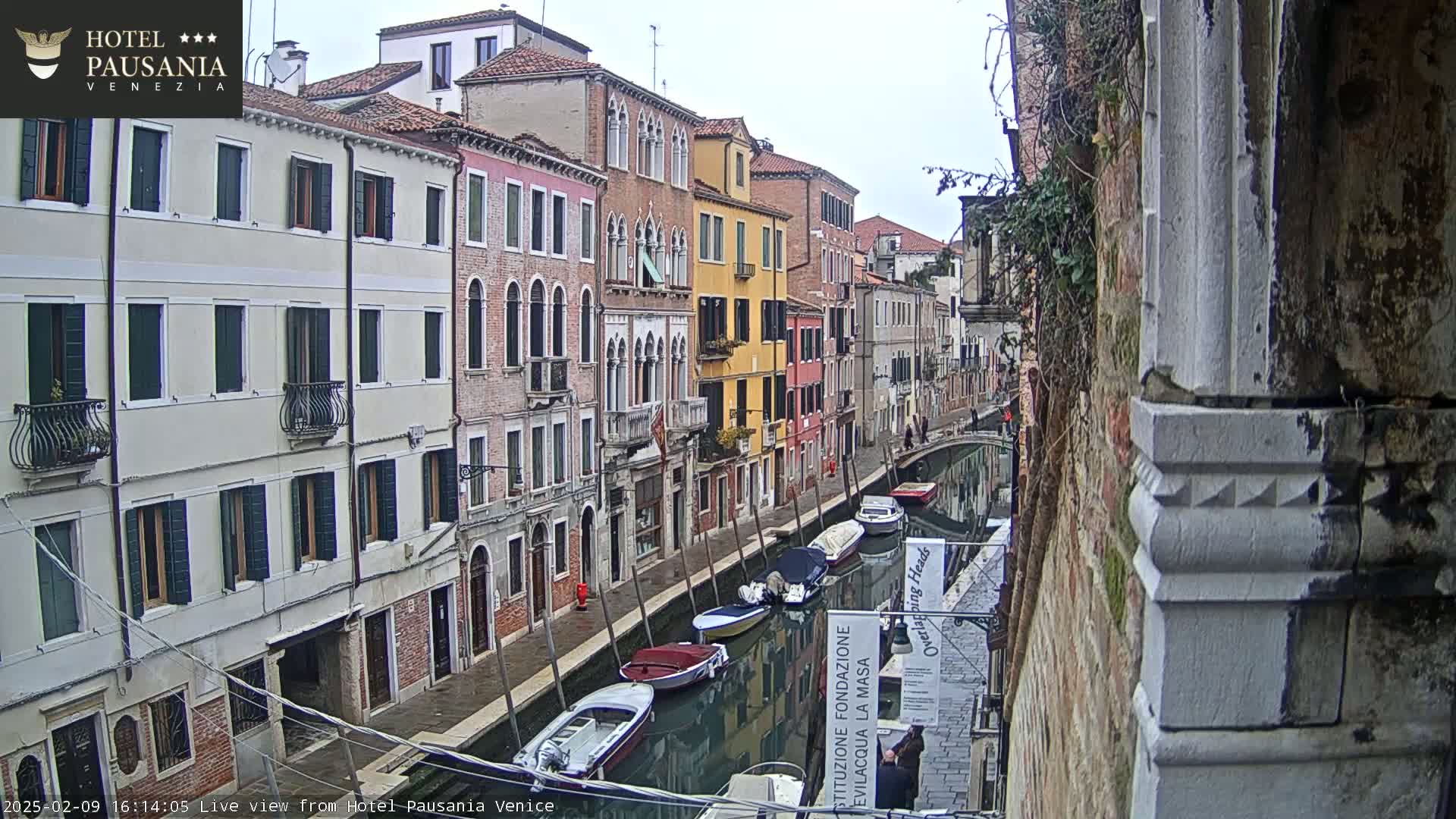 A canal in Venice, Italy, with several moored boats, is viewed from a building on an overcast day.