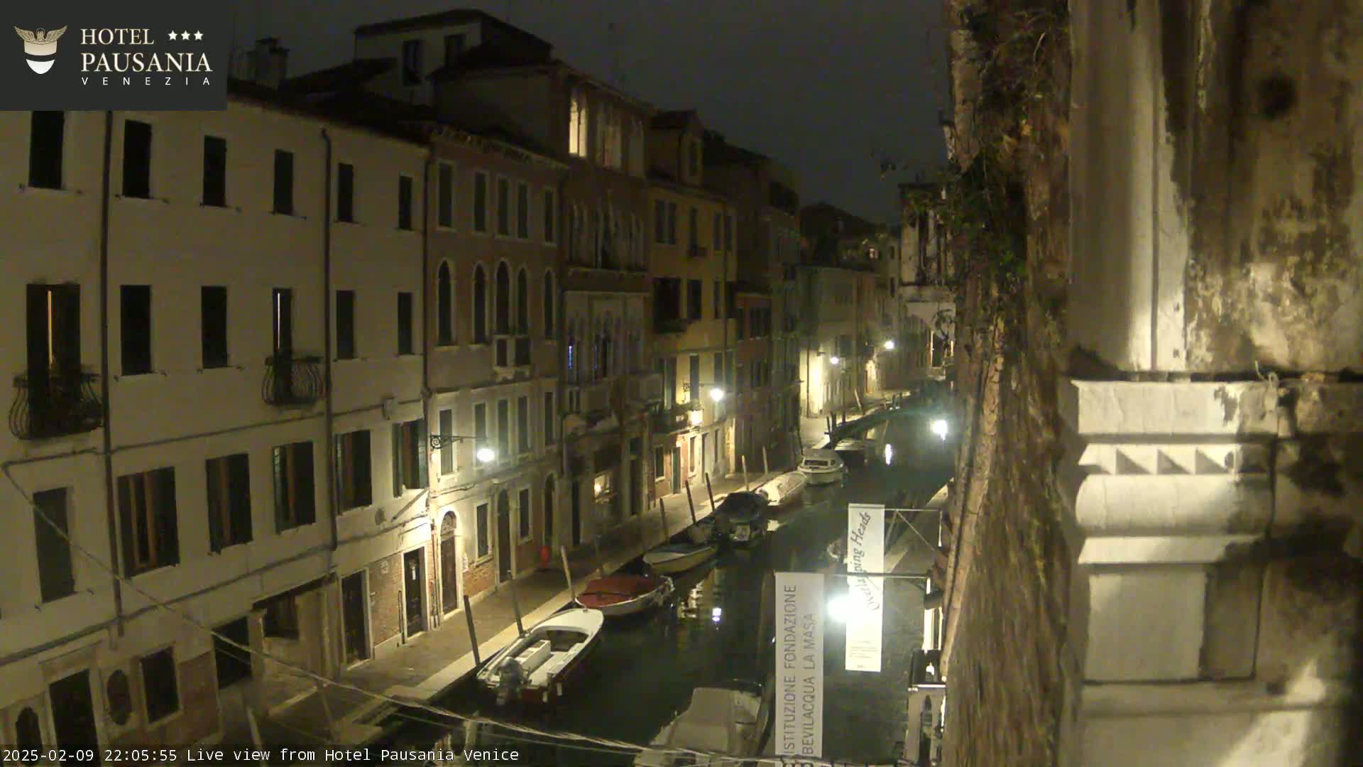 A nighttime view of a canal in Venice, with several boats moored along its banks and buildings lining either side.