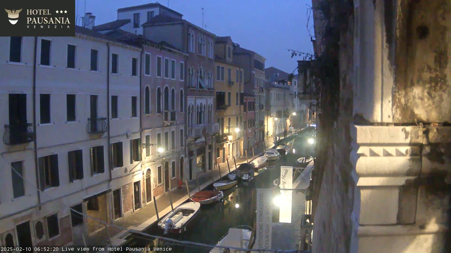 A dimly lit canal in Venice at twilight, lined with closely spaced buildings and several moored boats.
