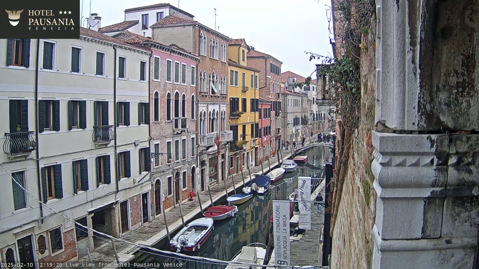 A narrow canal in Venice, Italy, lined with colorful buildings, is filled with several moored boats on an overcast day.