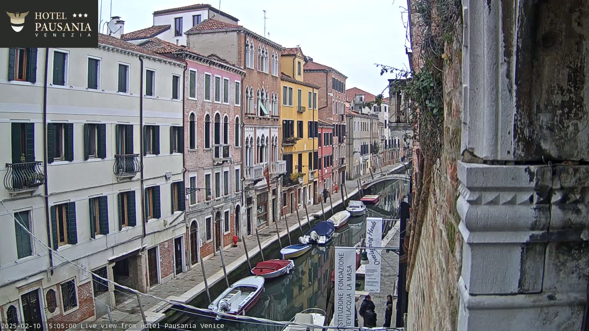 A canal in Venice, Italy, with colorful buildings lining its sides and several boats moored along its banks, under an overcast sky.