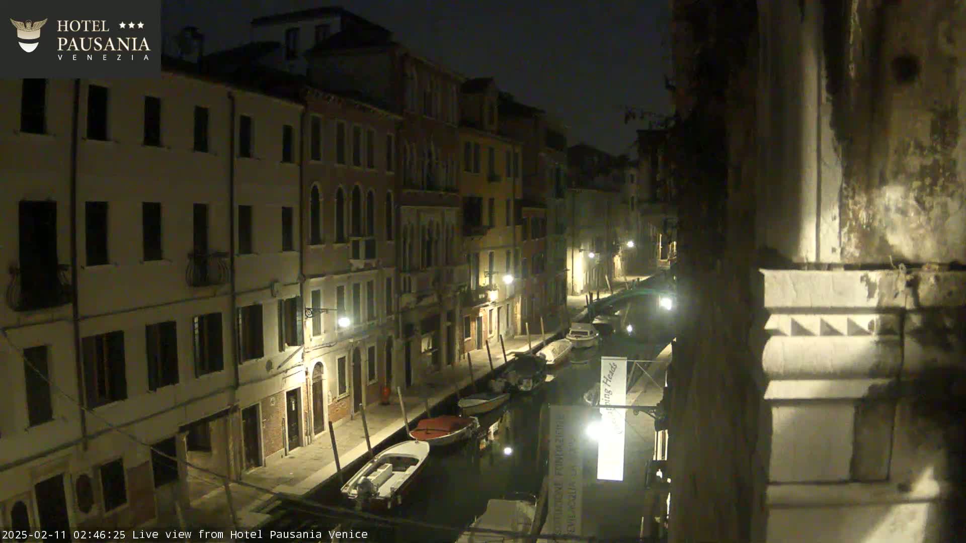 A nighttime view of a narrow canal in Venice, lined with buildings and a few moored boats.
