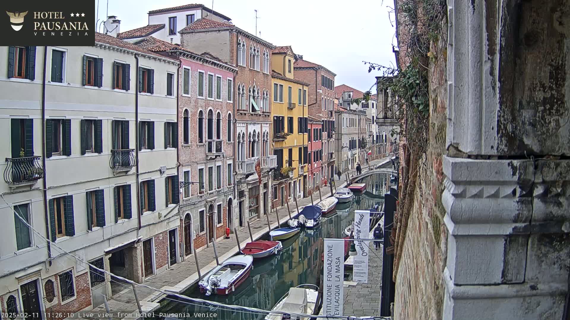 A canal in Venice, Italy, lined with old buildings on a cloudy day, is filled with several moored boats.